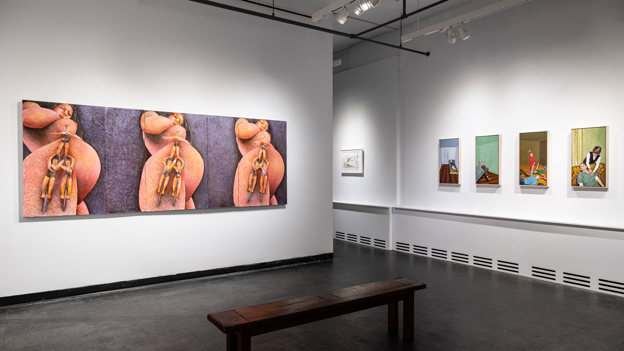 Installation view of an art exhibition with paintings. One painting is a triptych depicting a heavily pregnant figure. On the figure's leg, two unicyclists balance a third acrobat on their shoulders. On another wall is a series of four paintings depicting elders resting, exercising, and being palpated.