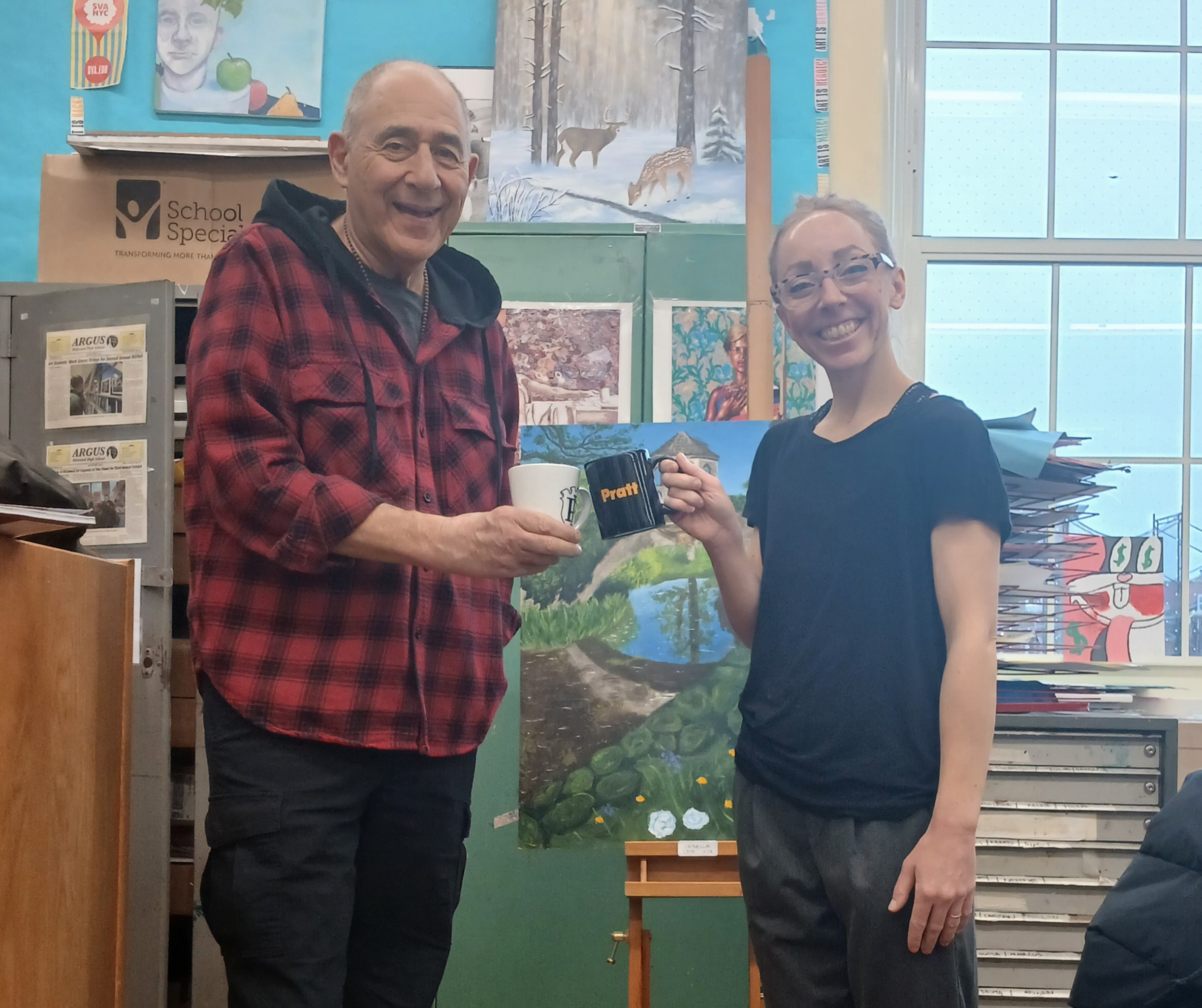 Alumni Barry Saines ’74 and Lauren Rocco (Danglo) ’12 pose in a colorful art classroom, smiling and holding Pratt-branded mugs