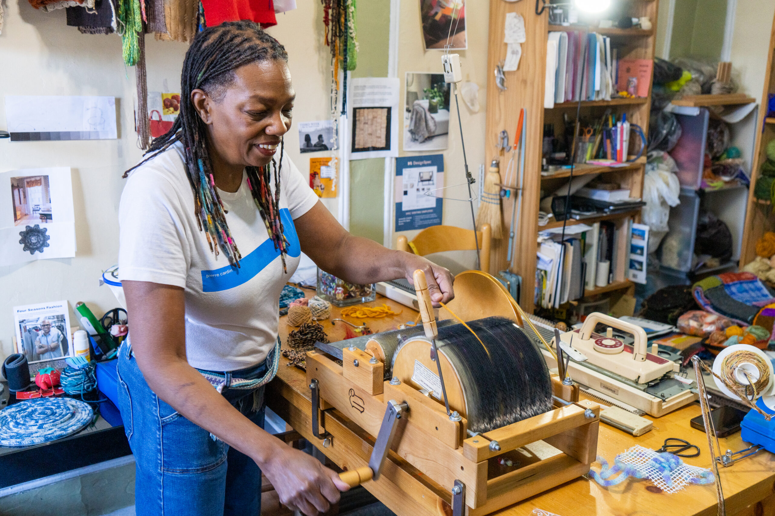 Sahara Briscoe smiles as she operates a drum carder, a tabletop, hand-cranked machine used to prepare raw wool and other fibers for spinning or felting.