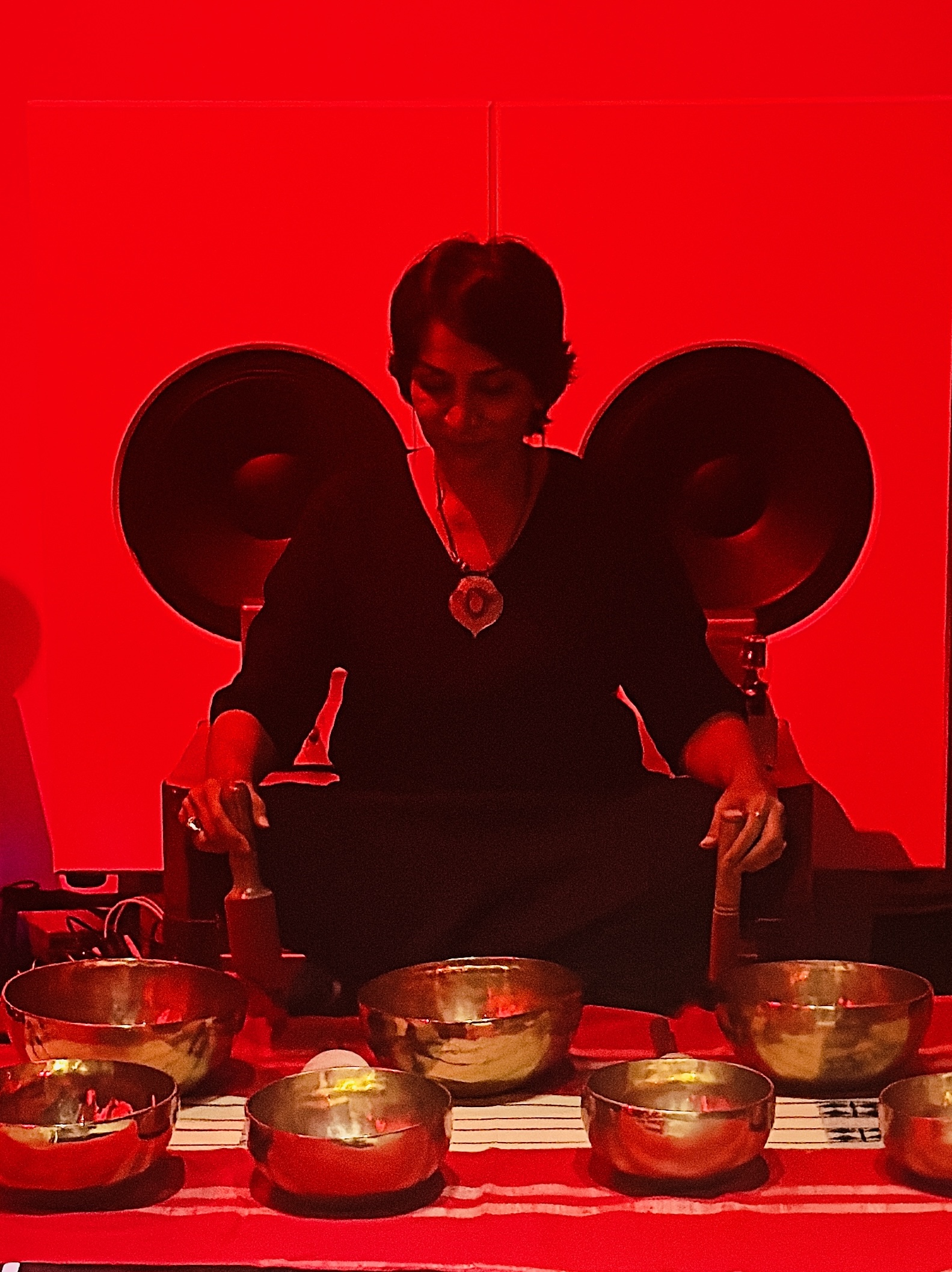 In a red room, alum Purvi Shah sits and plays singing bowls