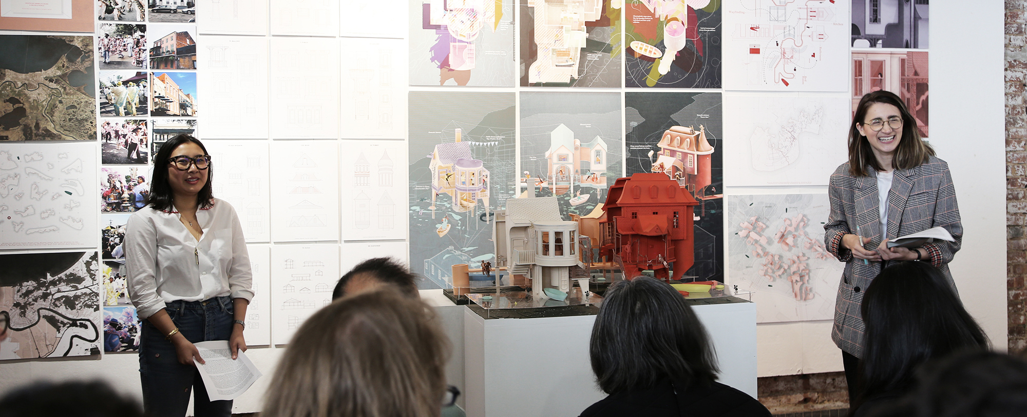 A person presents an architectural model in front of a group of attentive spectators.