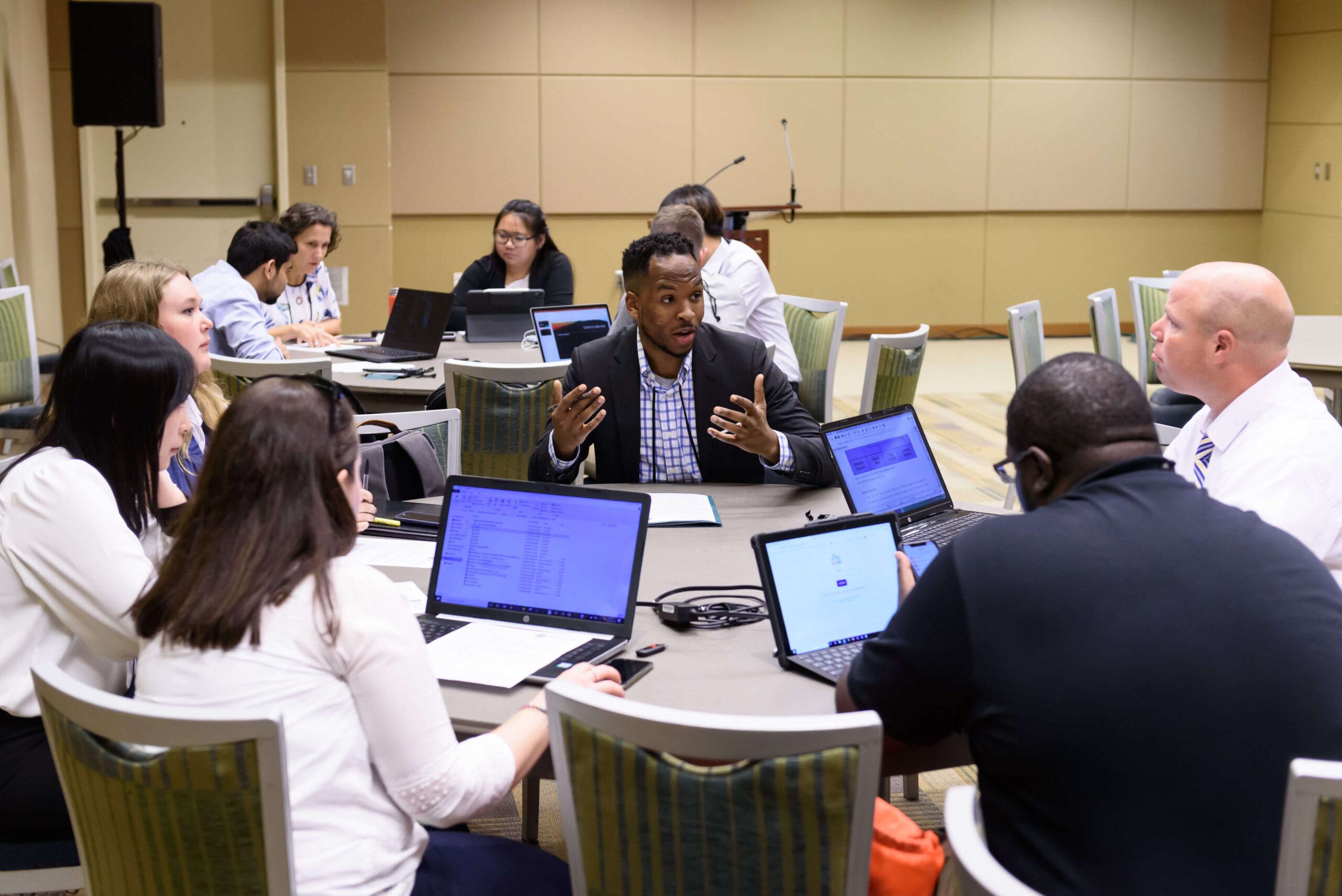 A group of people sit around a table with their laptops out as they discuss.