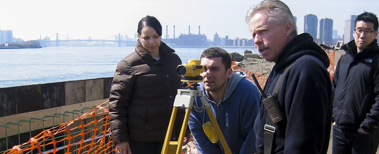 Construction management students are guided on the use of a yellow topographic device as an instructor speaks to them.