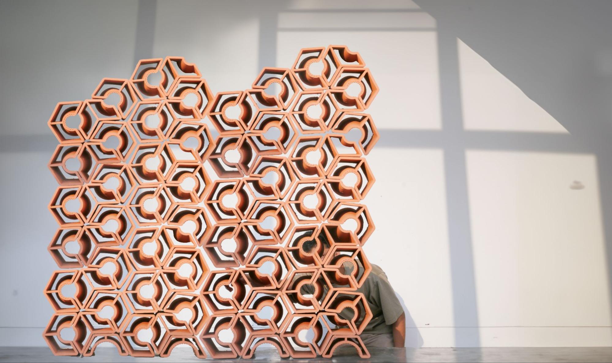 model of structure built in a honeycomb formation in foreground, student against wall looking at model in background