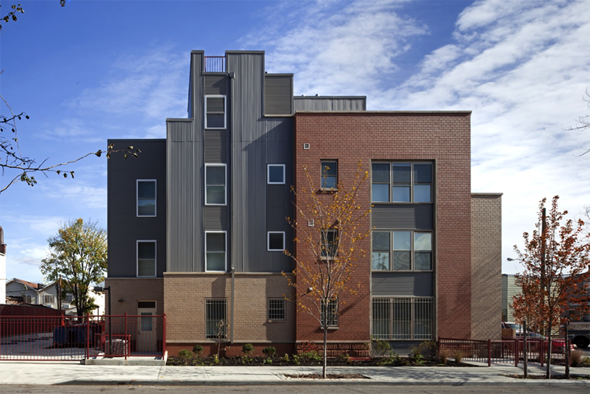 Image of a building's façade made out of red bricks with two young trees standing in front of it.