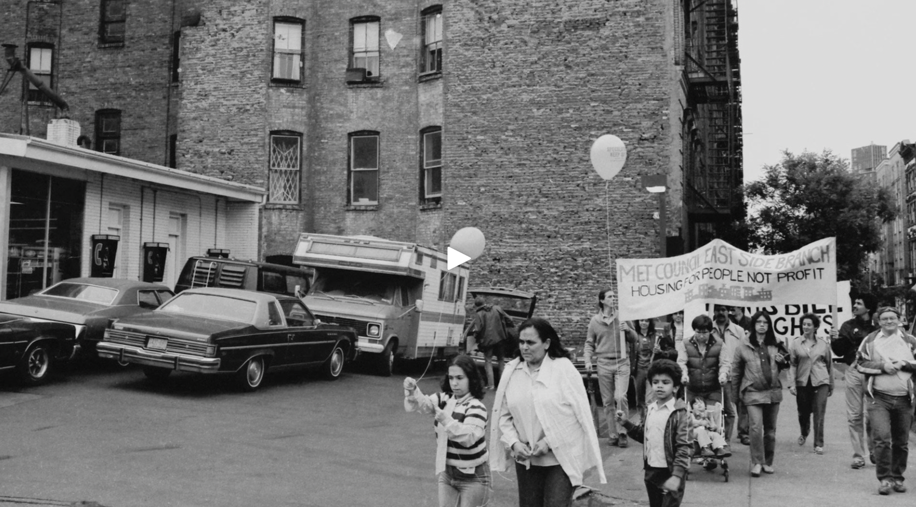 A black and white image of a protest, where one of the large banners read the phrase 