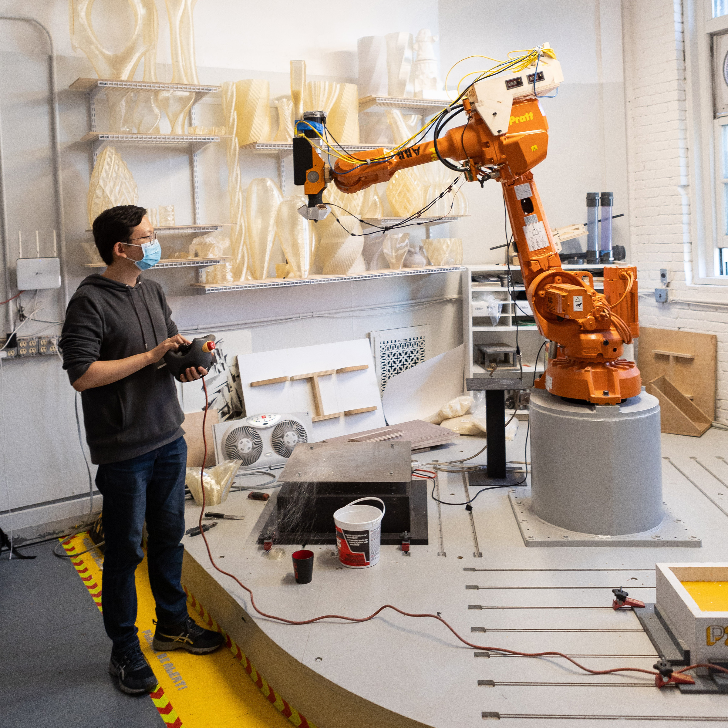 A person stands in a studio next to a large, orange robotic arm