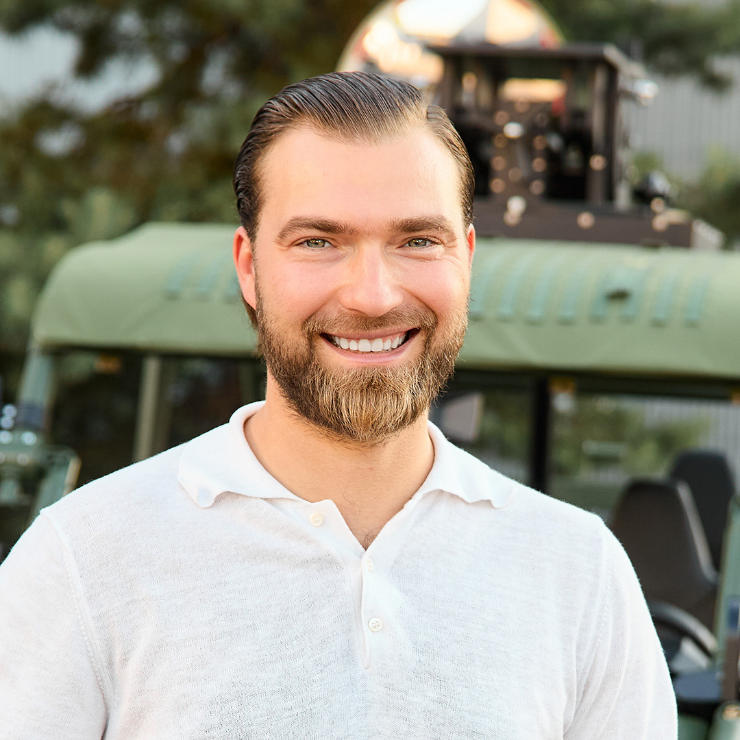 A smiling white man with blond hair and a beard wearing a white shirt.