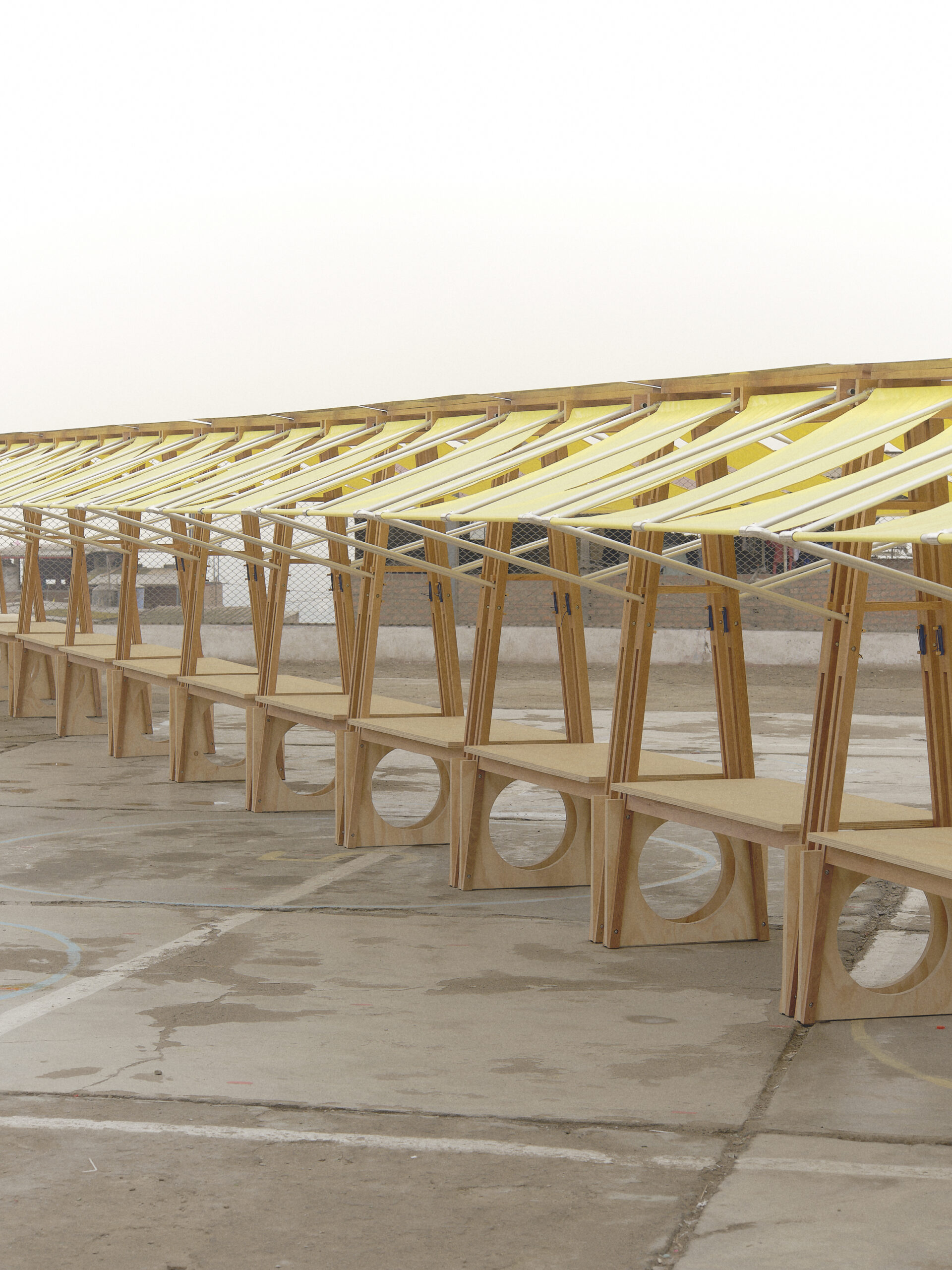 A close-up view of wooden structures with circular cutouts at the base, supporting bright yellow canopies stretched by white poles.