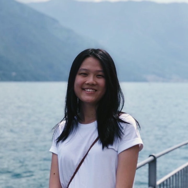 Portrait of a woman standing in front of a body of water in a white shirt.