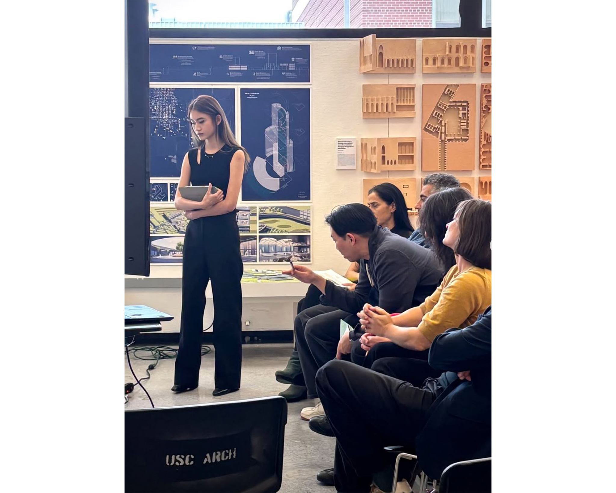A student presents her architectural project during a final review, as a panel of critics looks on attentively.