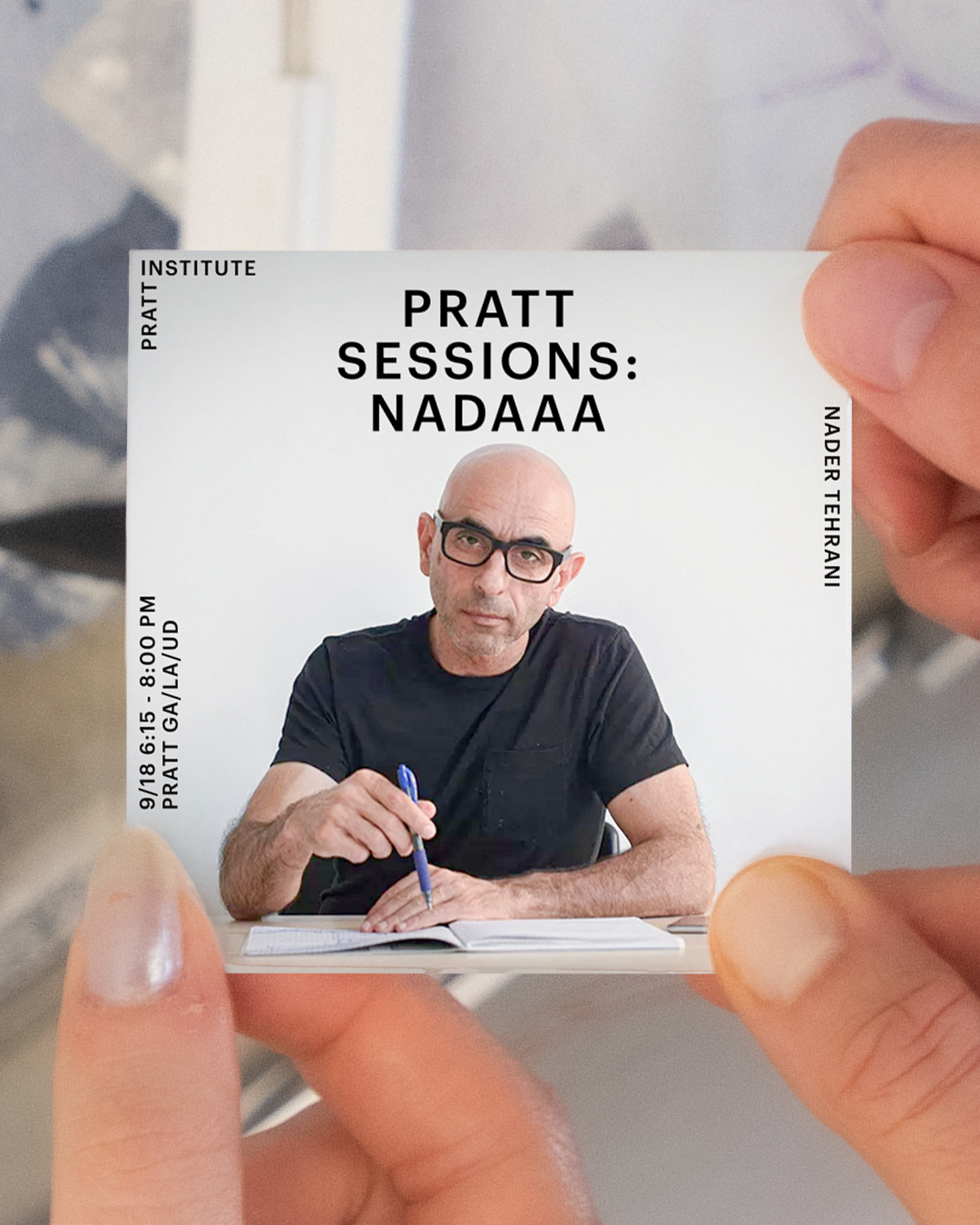 A person holds a card featuring the text "PRATT SESSIONS: NADA" with details about an event dated 9/18 from 6:15 to 8:00 PM at Pratt Gallery. The individual is sitting at a desk, writing in a notebook with a blue pen, wearing a black t-shirt, and has glasses. The background appears blurred with abstract shapes.