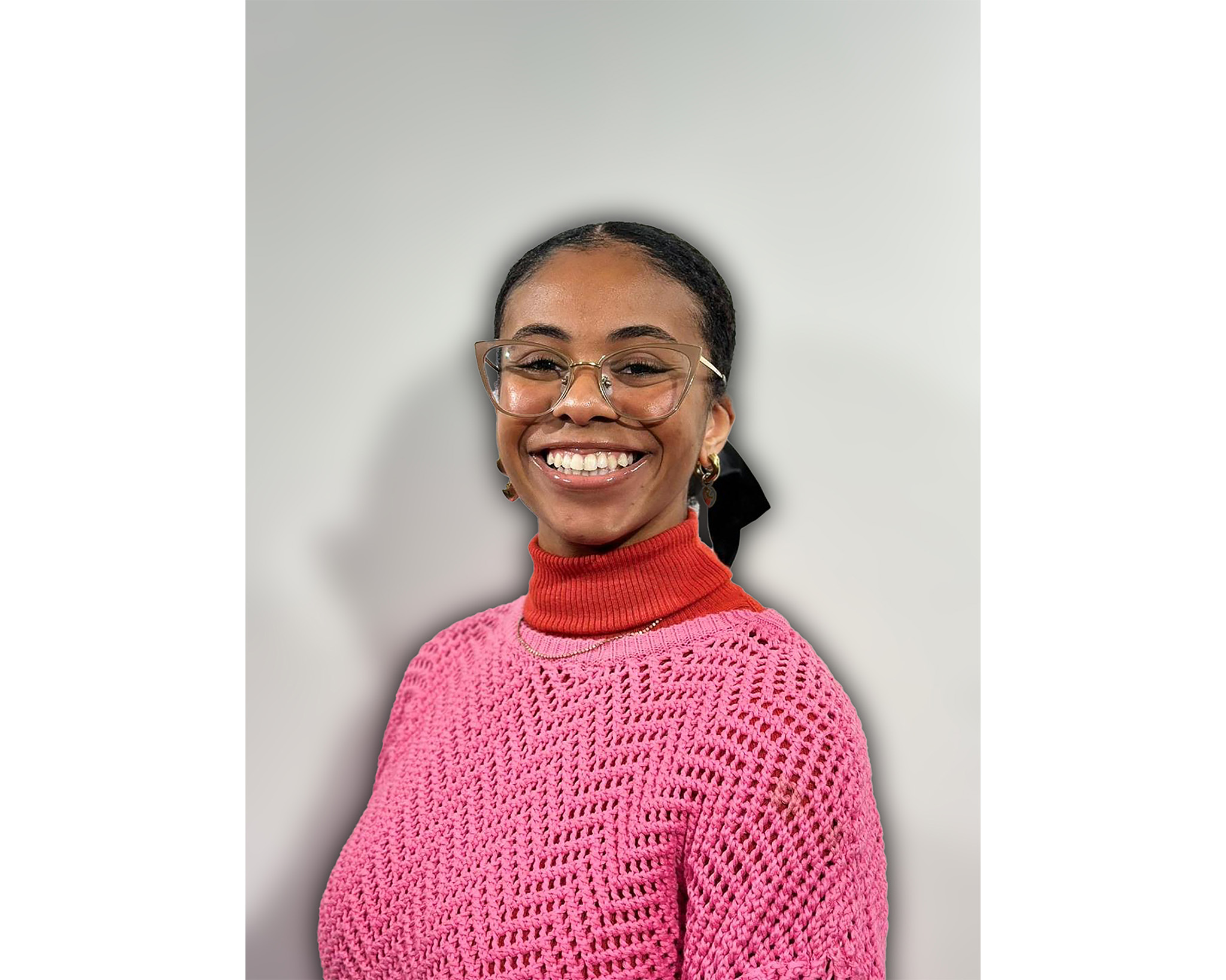 A student wearing glasses, an orange turtleneck, and a pink sweater smiles at the camera.