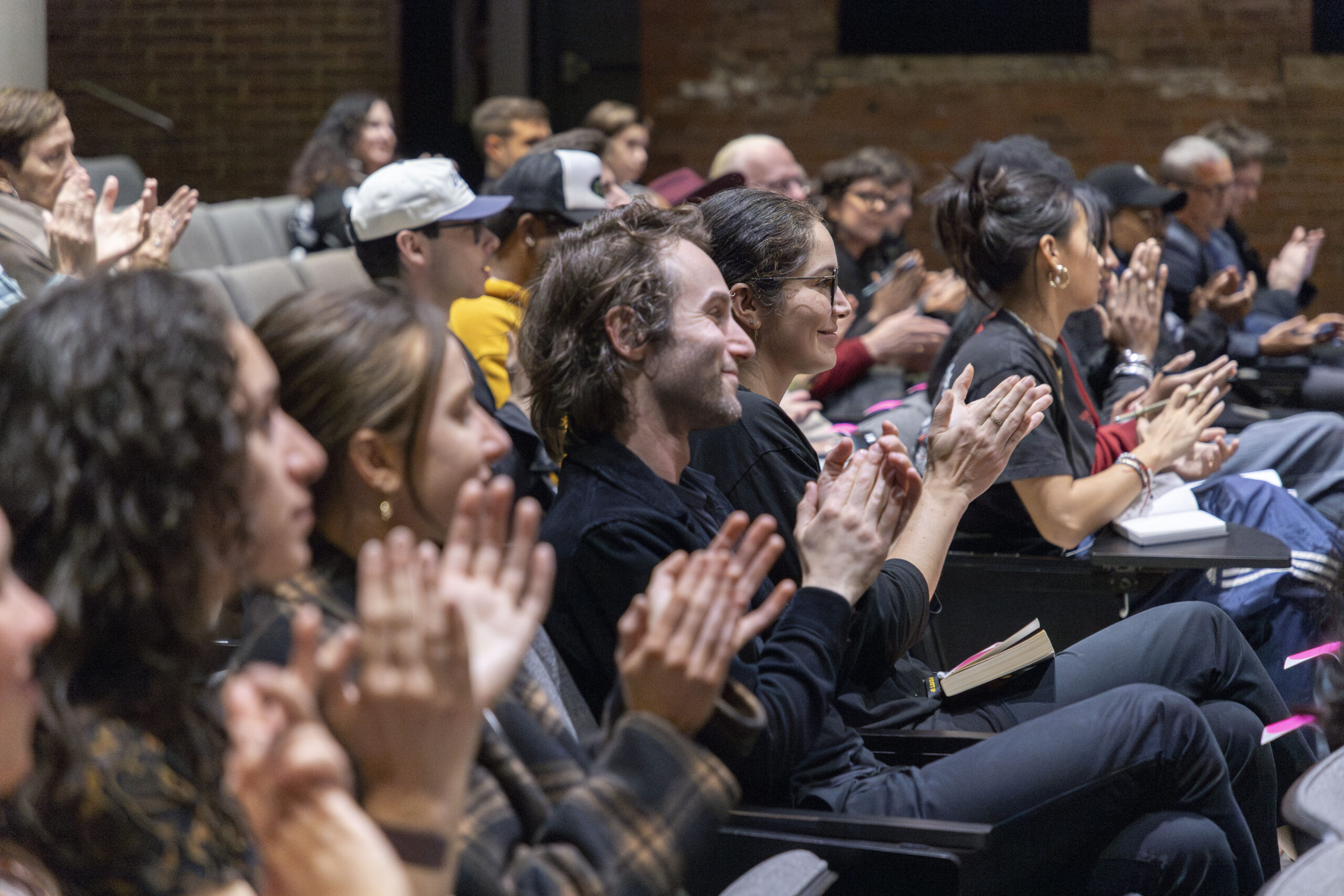 A computer monitor displays a presentation titled "Lessons from the African American Garden," featuring an image of a woman smiling and holding books. In the foreground, a microphone and part of a wooden podium are visible. The background captures an audience seated and looking towards the presenter.