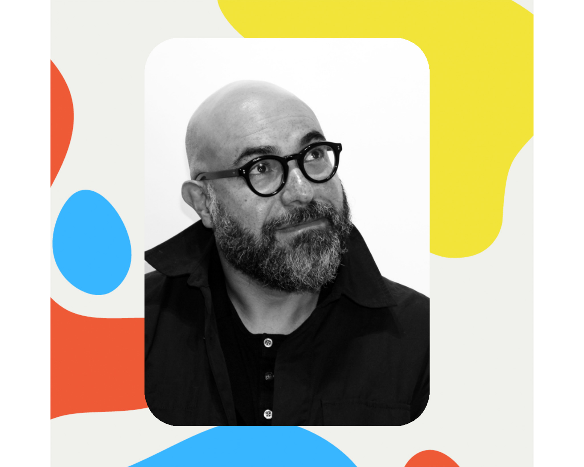 A close-up portrait of a bald man with a thick beard and glasses, looking upwards with a thoughtful expression. He wears a dark shirt and has a black jacket collar visible. The background features colorful abstract shapes in red, blue, and yellow.