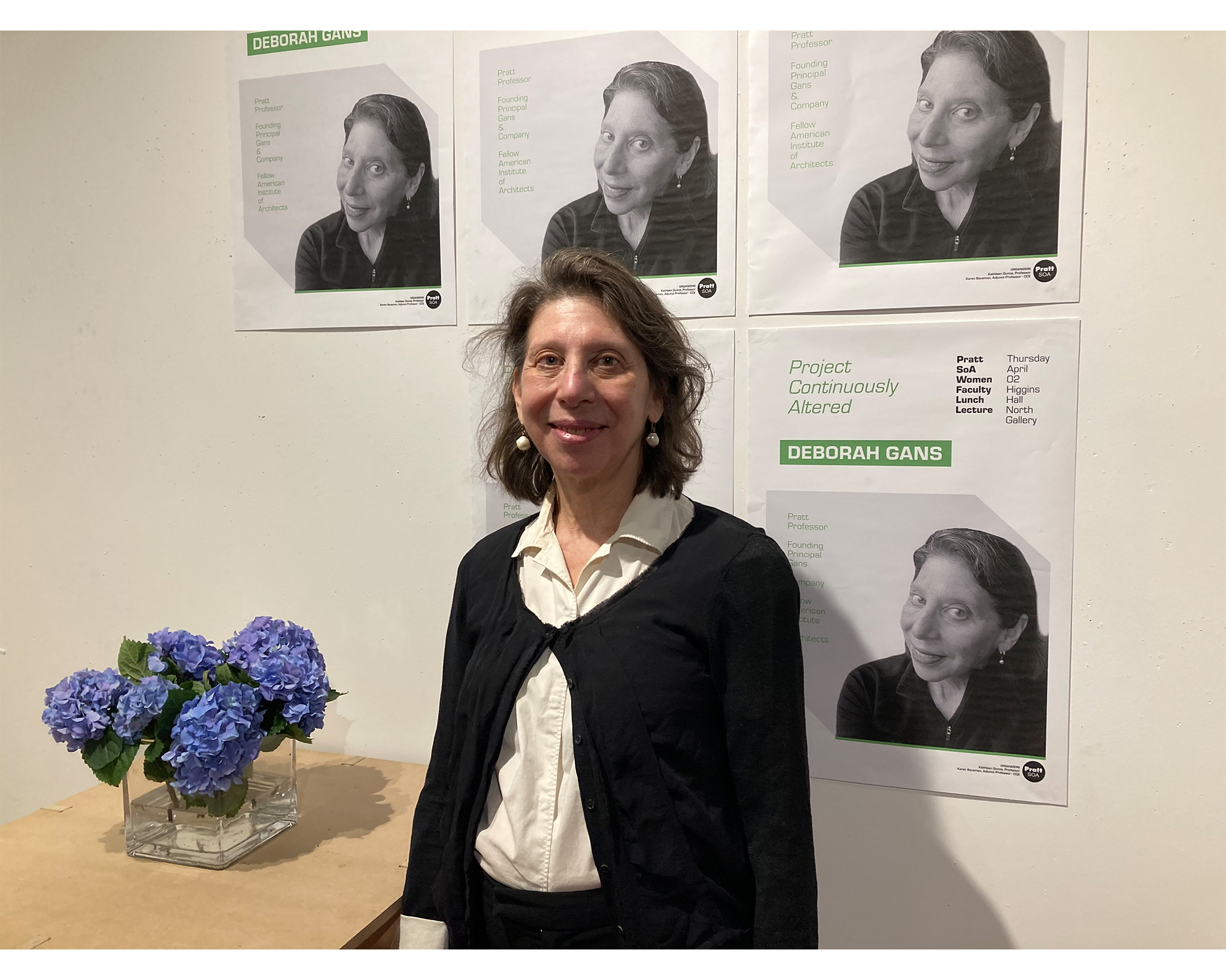 A faculty member stands beside a bouquet of flowers and a wall of posters.