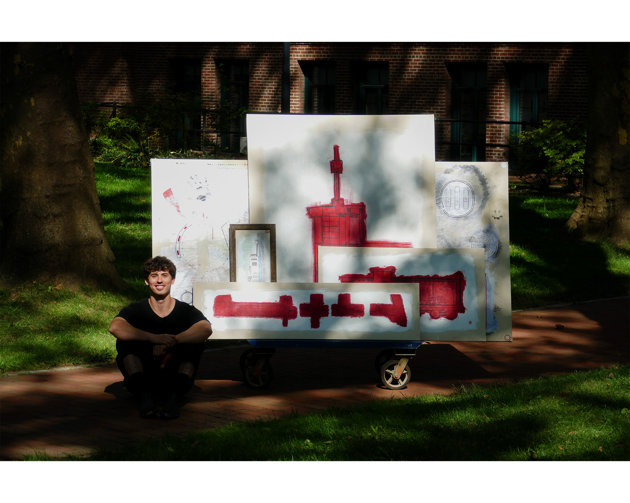 A student seated outside in sunlight in front of architectural drawings.