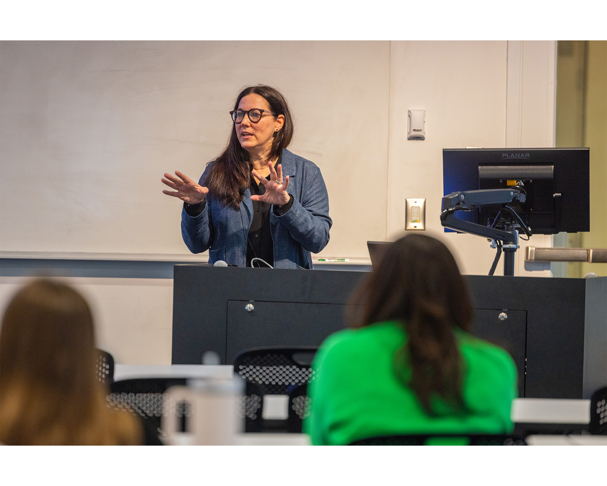An architect in a blue jacket is speaking in front of a lecture hall.
