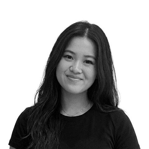A smiling young woman with long, straight black hair is standing against a white background. She is wearing a simple black t-shirt and is looking directly at the camera, exuding a friendly demeanor.