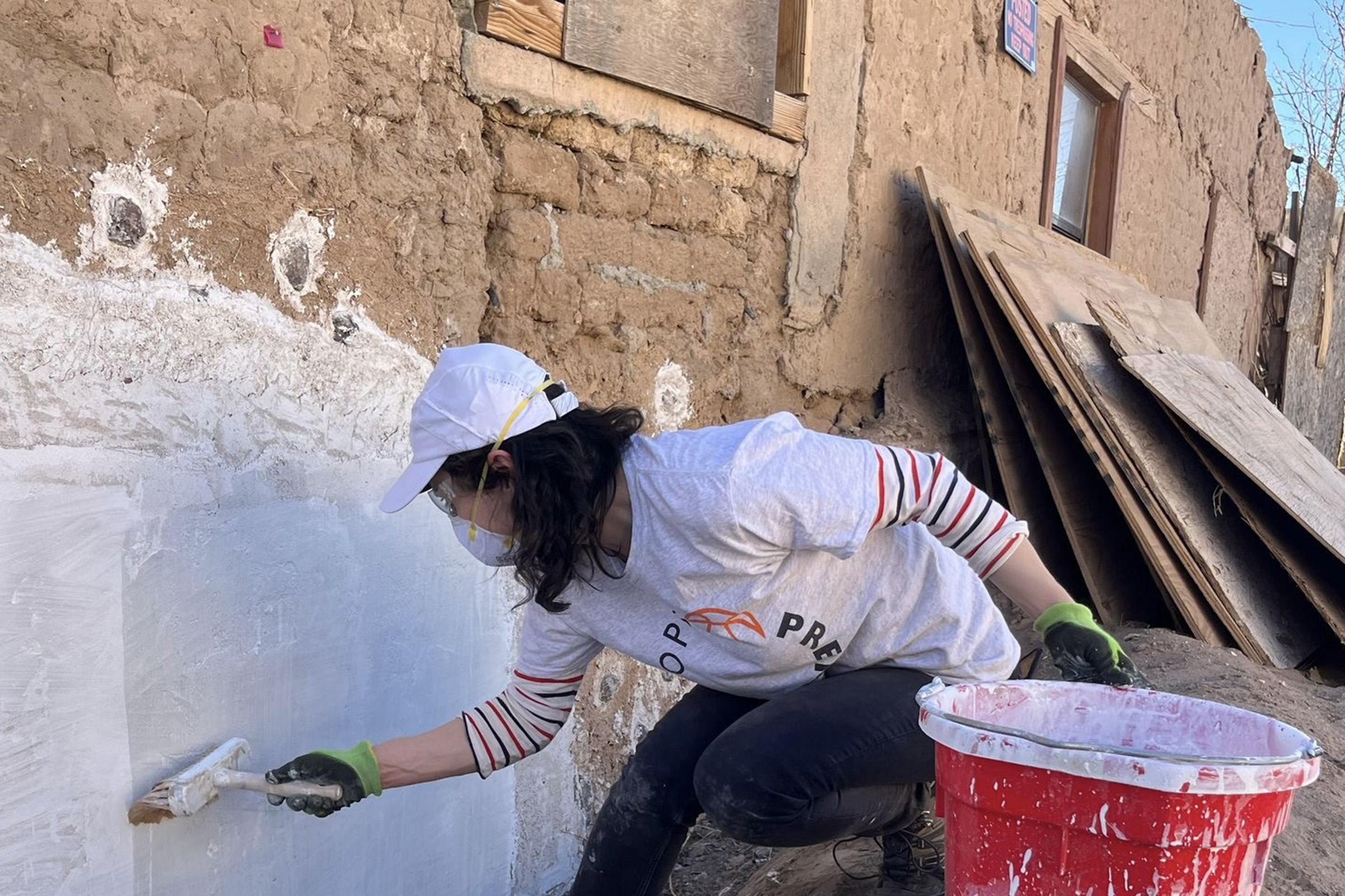 TatianaMurat_NM_Limewash.jpg — A student wearing protective equipment limewashes an adobe building.