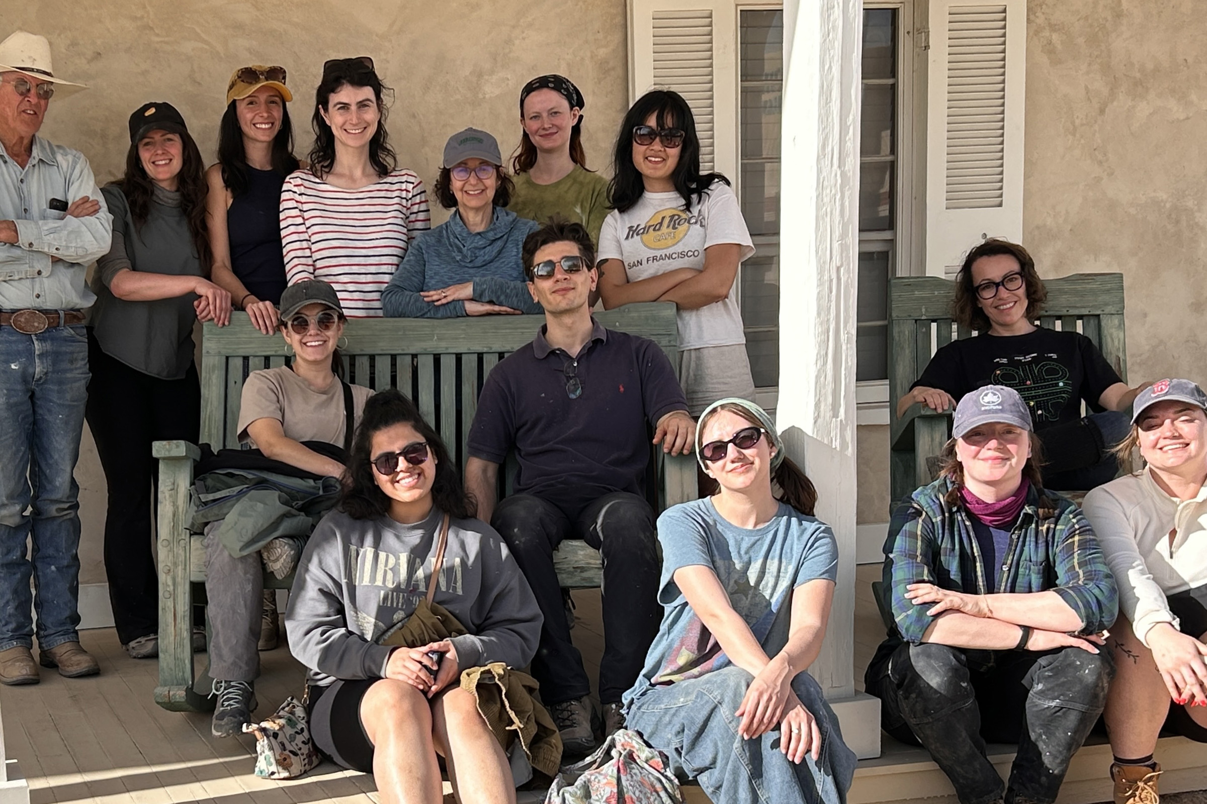 roup of fourteen people poses together for a photo on the porch of an adobe building.