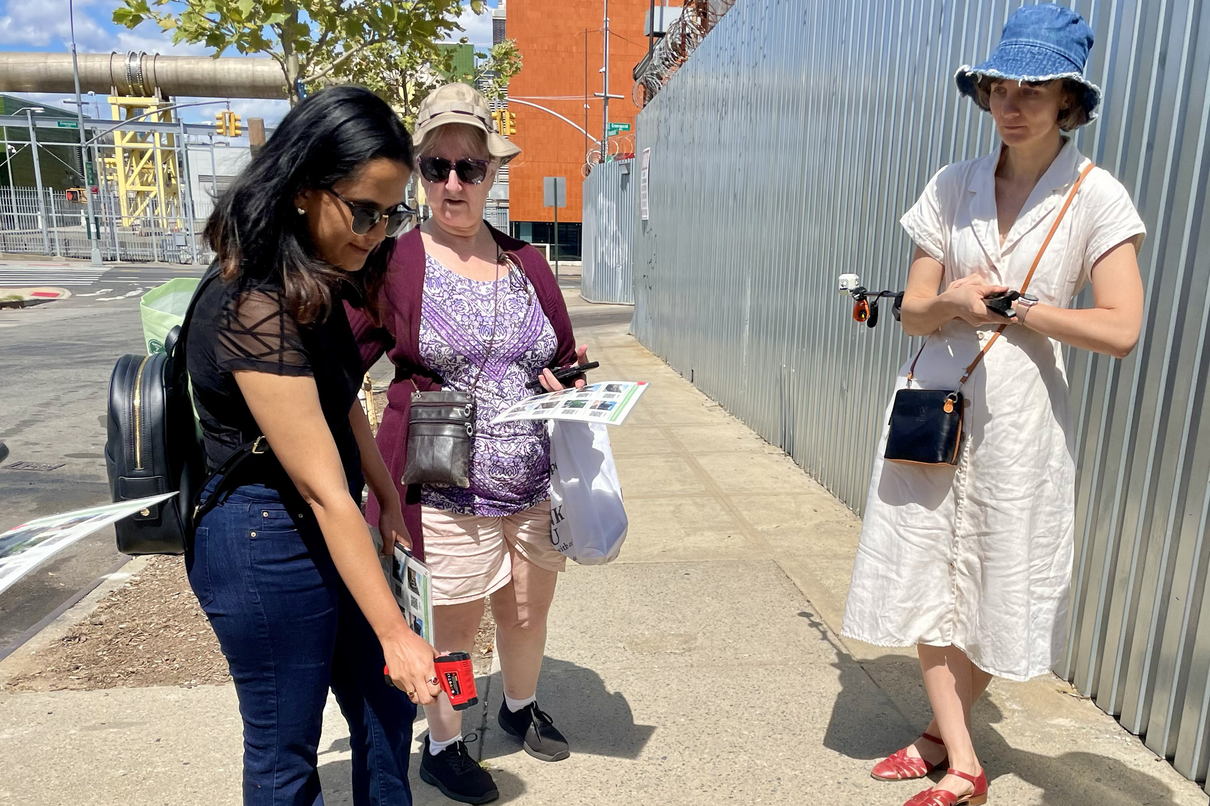 A student points a heat sensor at the sidewalk as two individuals watch.