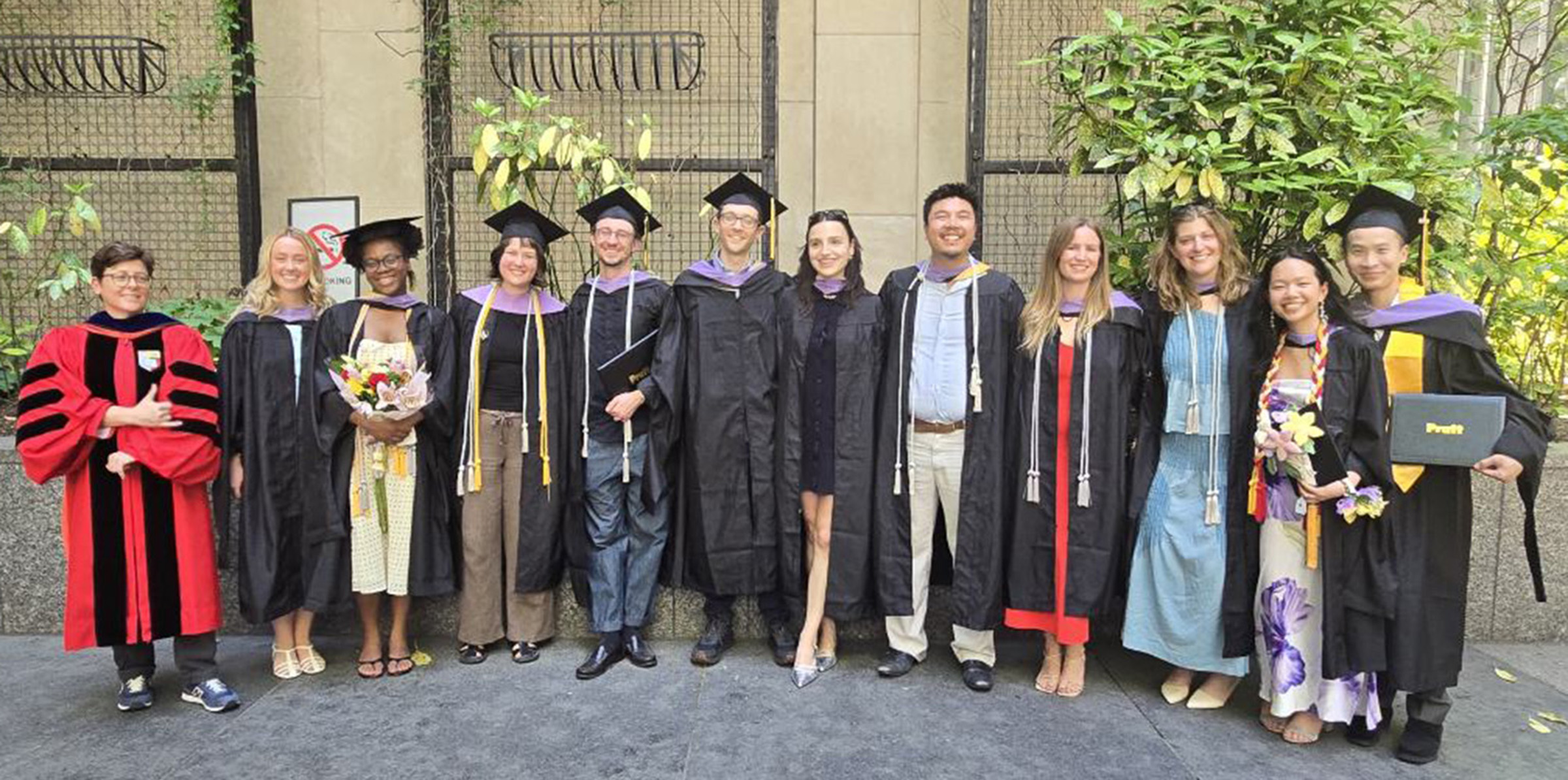 A group of eleven students in cap and gowns pose with a faculty member also wearing regalia.