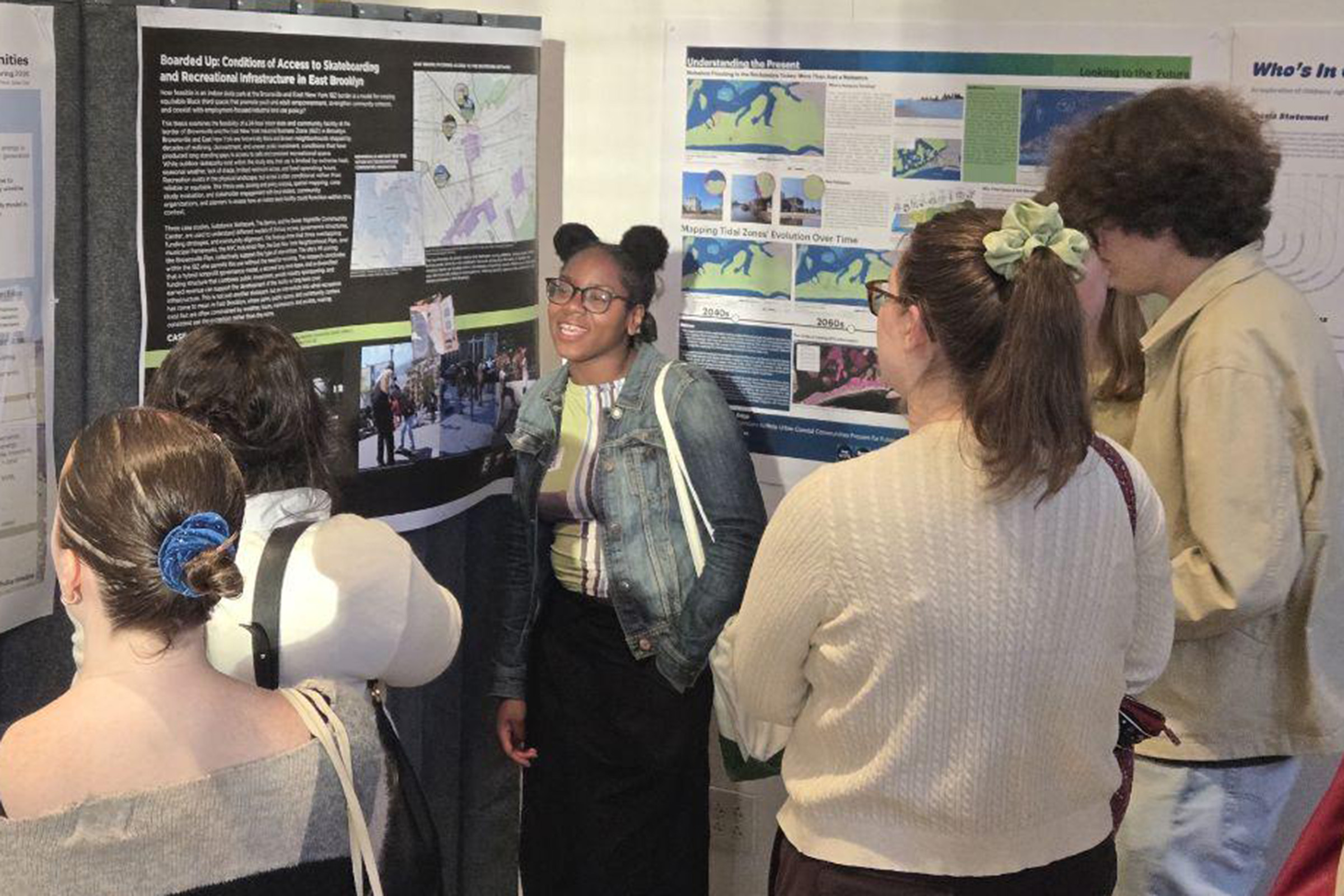A student standing in front of their research poster, talking to a group of fellow students.