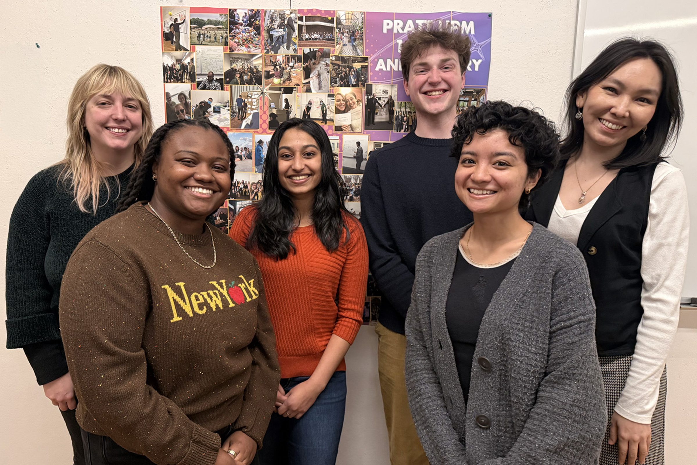 A group of six students poses together in front of a poster in a classroom.