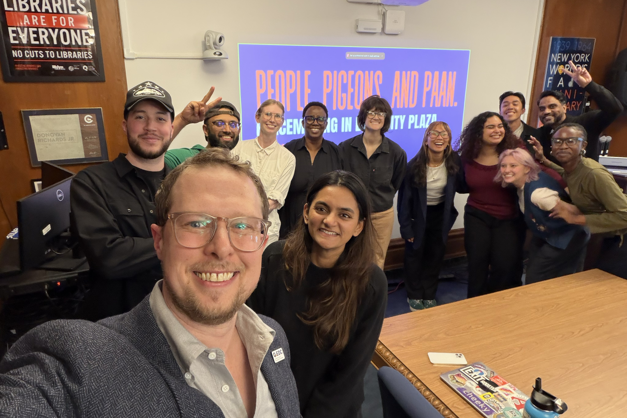 A group of thirteen individuals poses together in front of a slide presentation for a studio class.