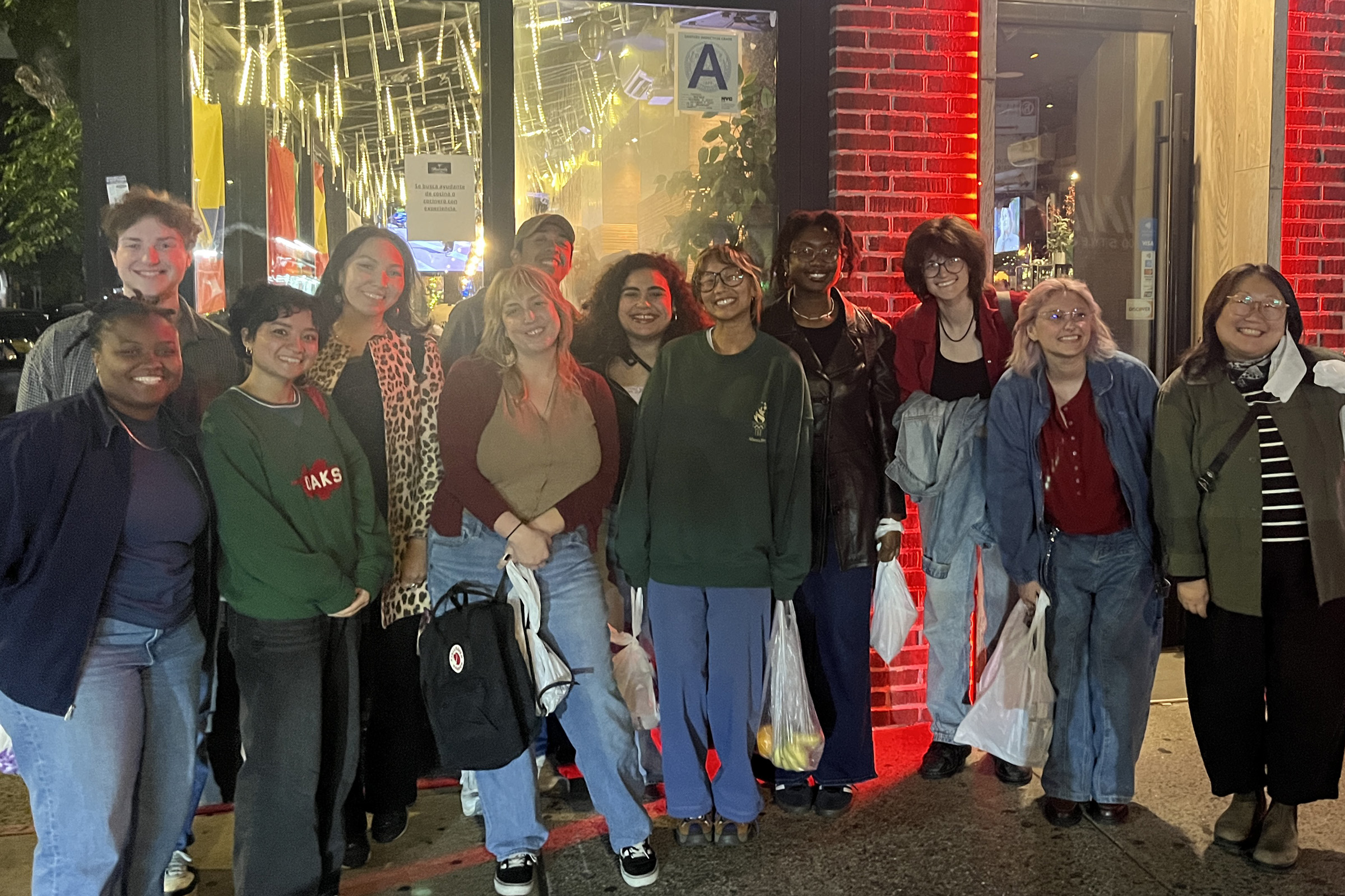 A group of twelve smiling people poses together outside a restaurant.