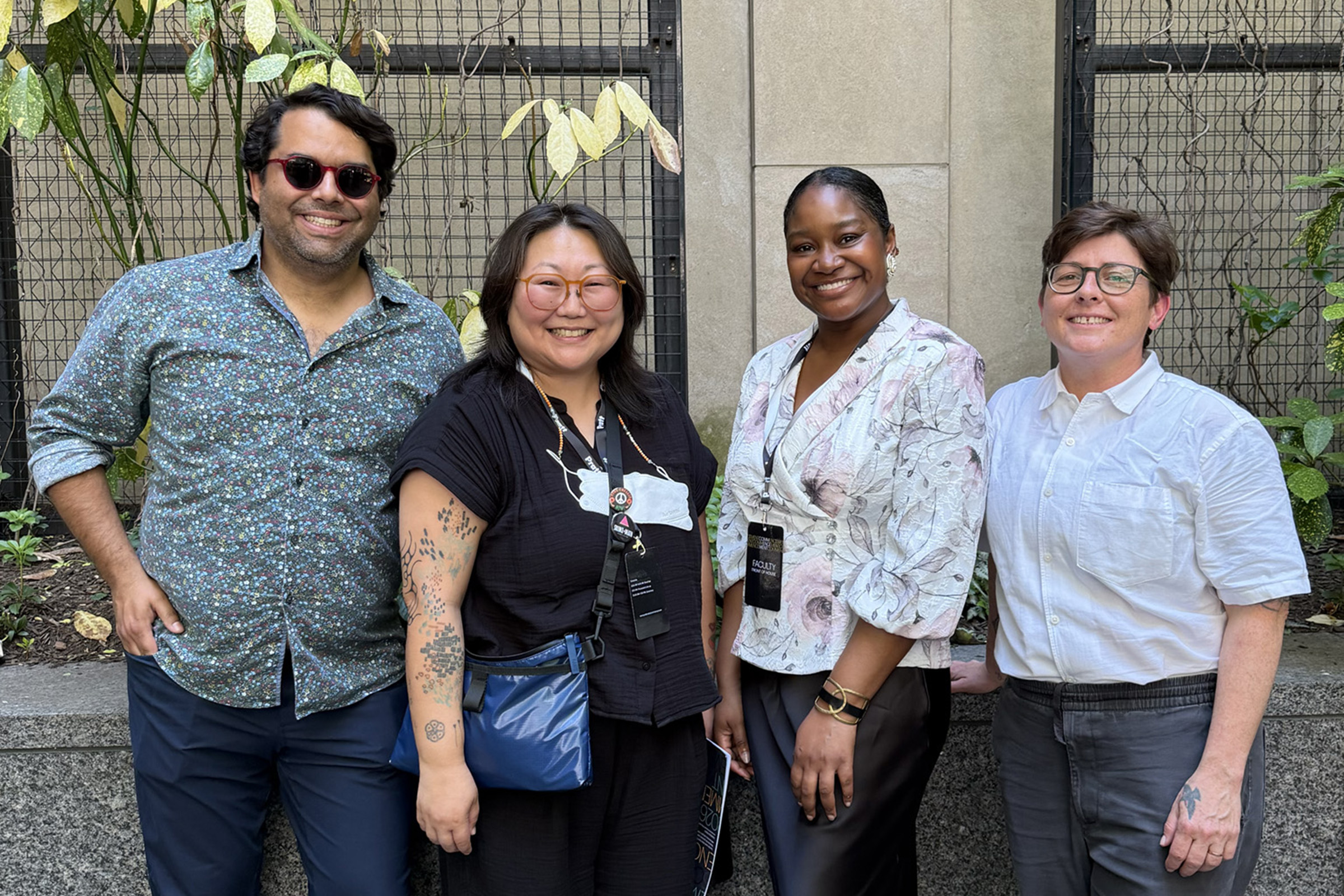A group of four individuals poses for a photo outdoors against a backdrop of plants.