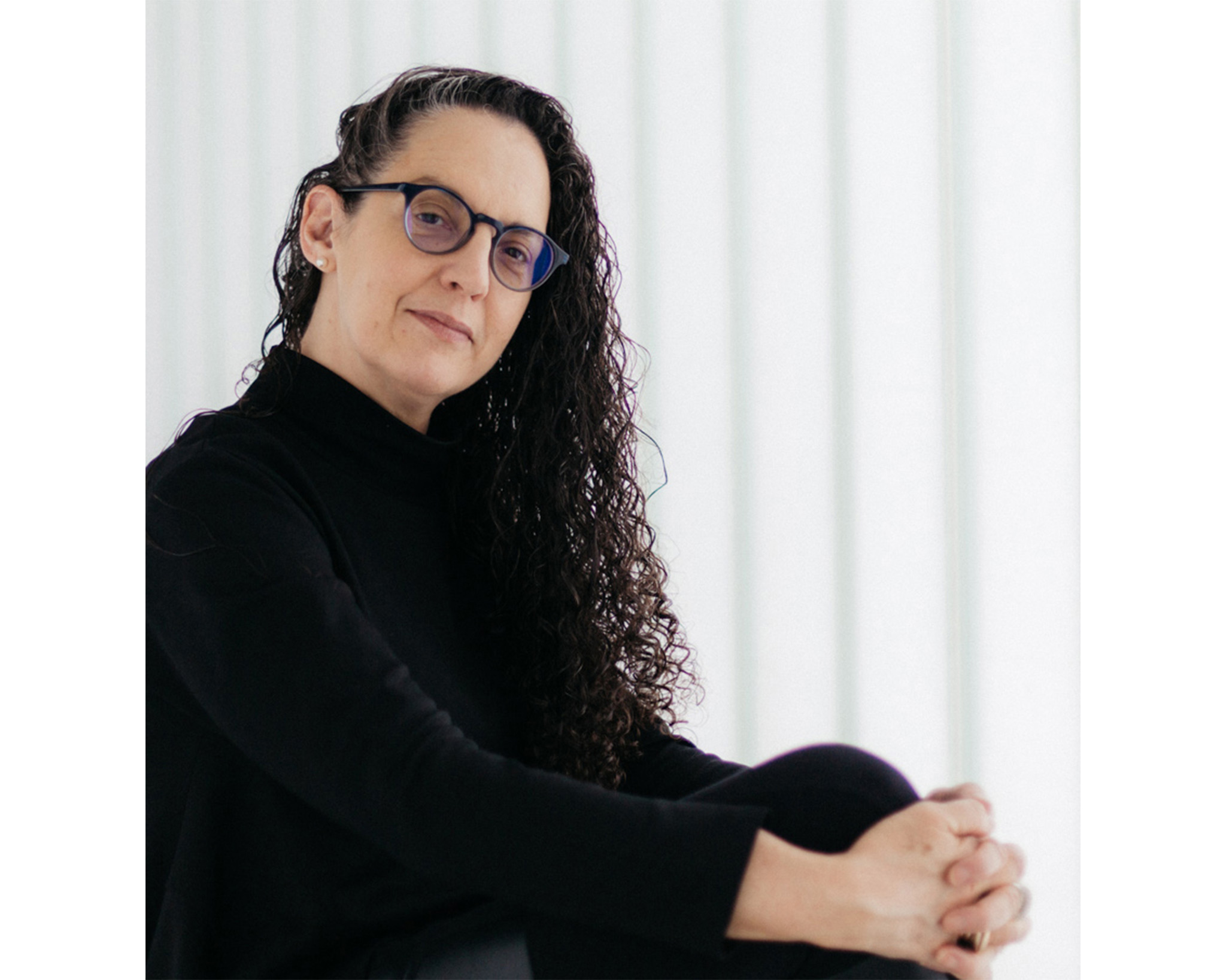 Woman with glasses wearing all black poses against a white background.