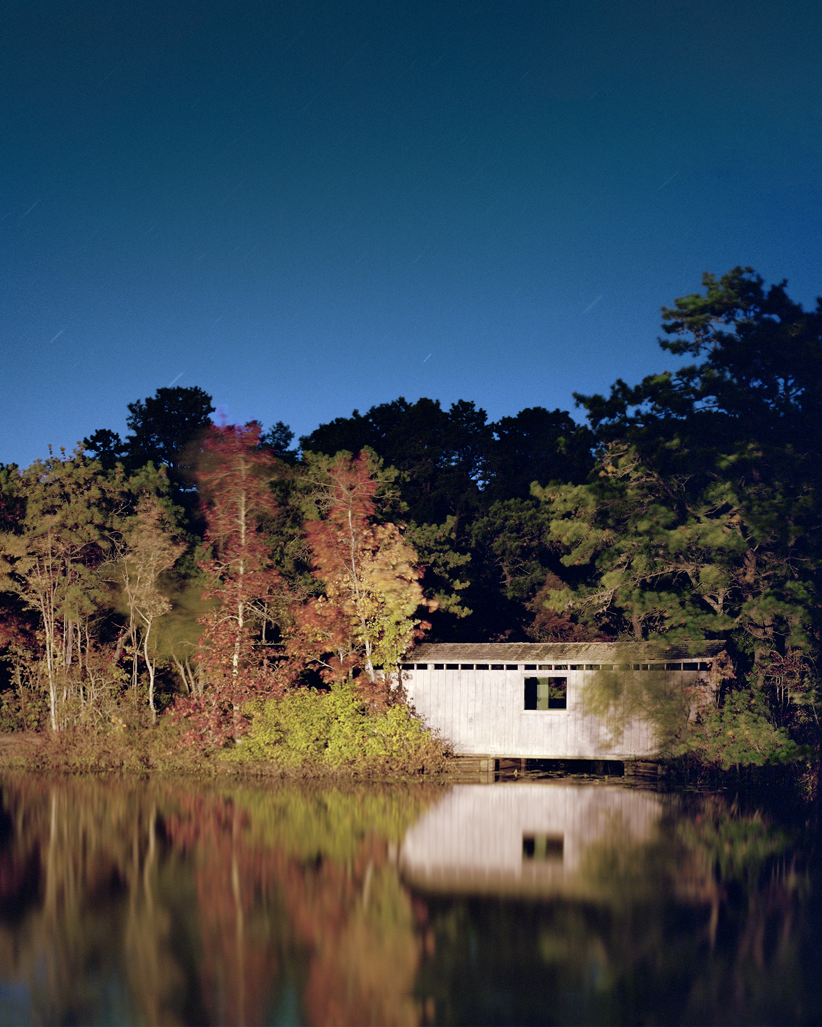 lakehouse at dusk, large spotlight shining on house, forest in background, lake and house in the foreground