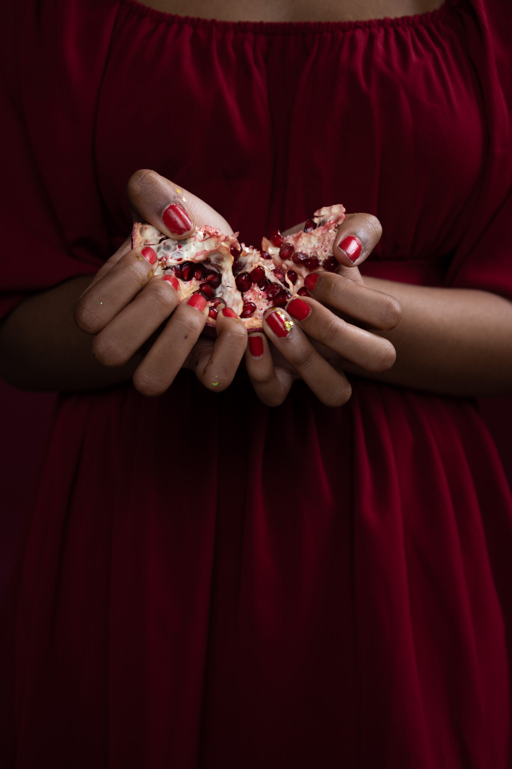 two hands, with nail polish, holding rocks, against a black background, only hands and wrist