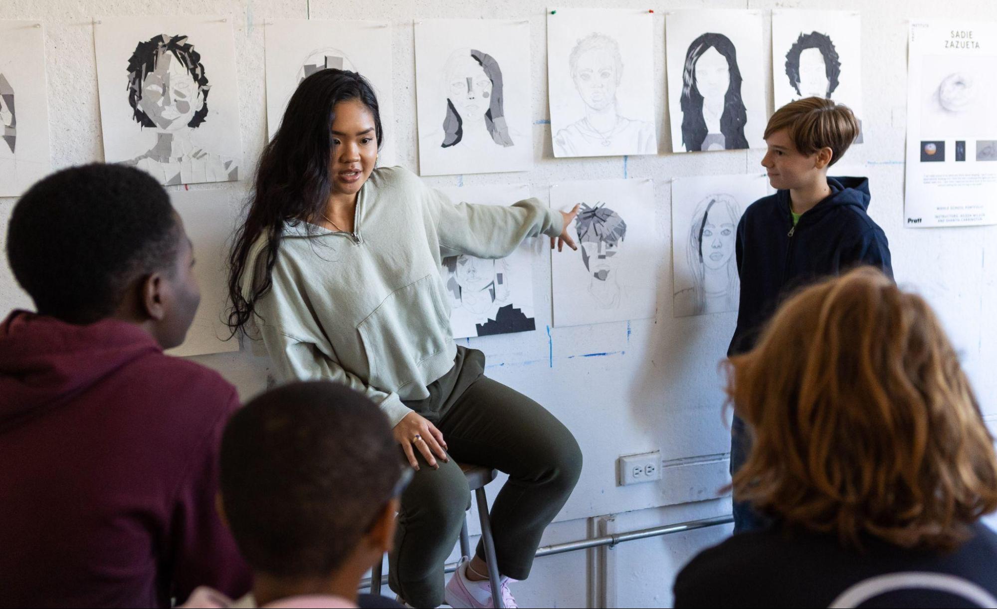 A student-teacher in Saturday Art School discussing work with middle school students.