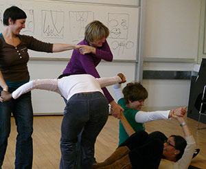 A group of students practices dance therapy with the assistance of an instructor wearing a purple cardigan