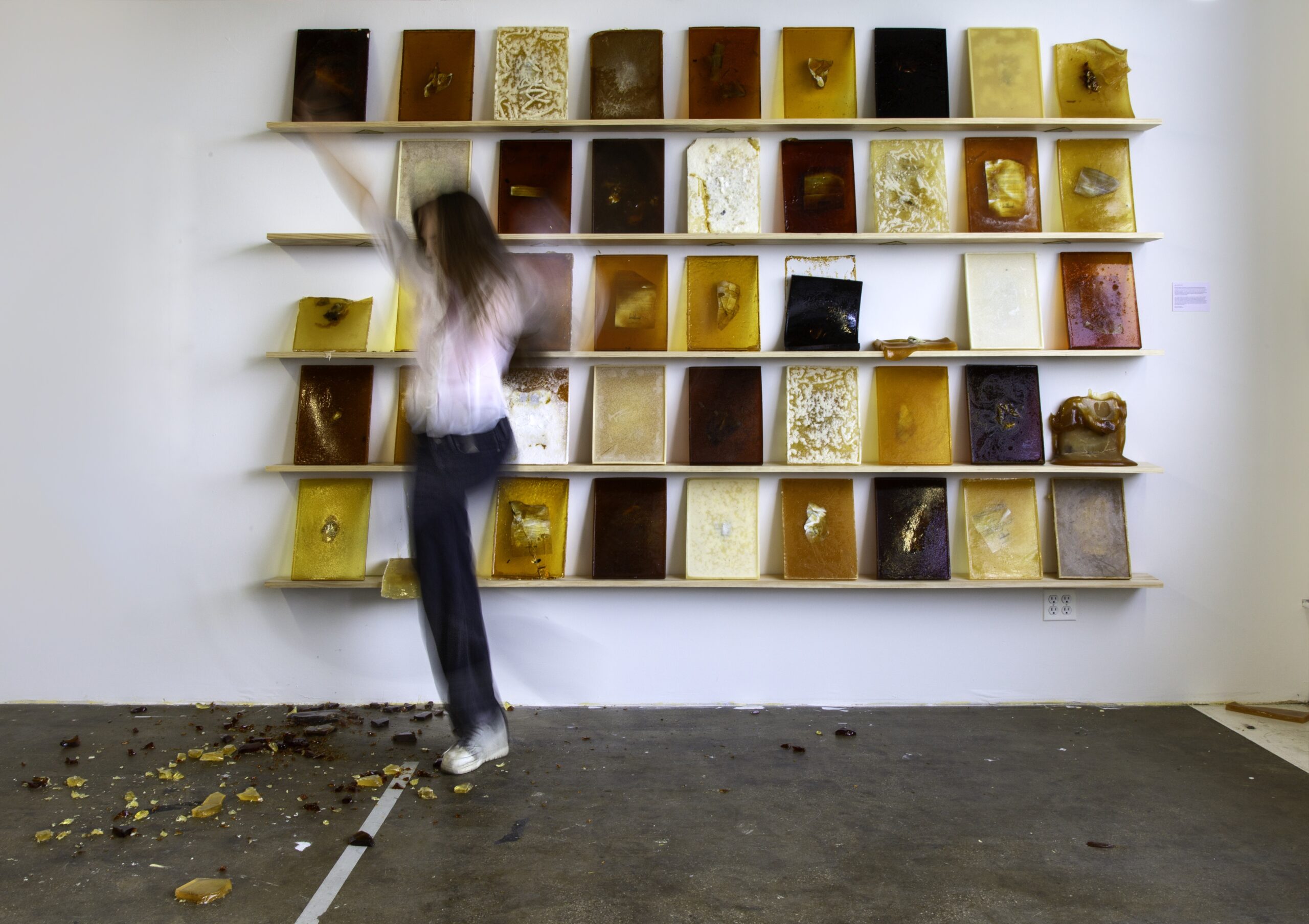 A photograph of a wall with many books on shelves facing out to the viewer. There is a person in movement in front of the shelves. They are blurry in the photograph.