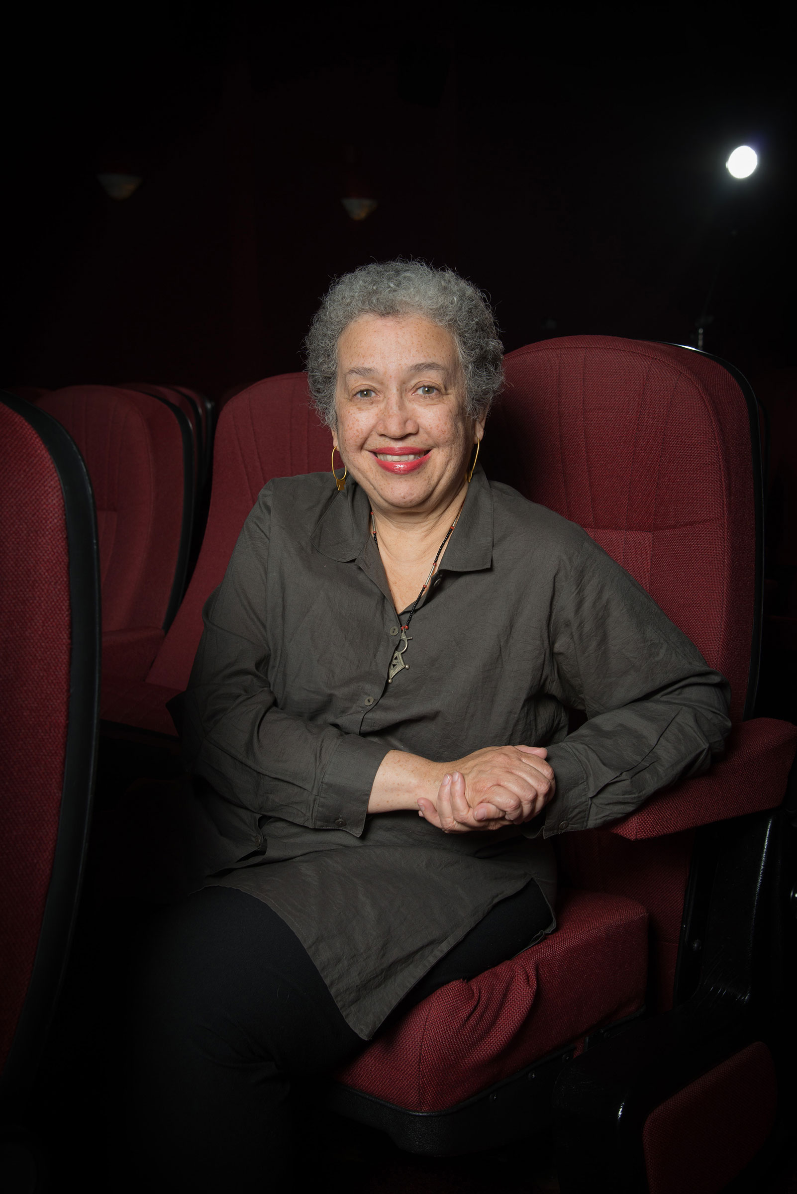 A woman with gray hair in a gray dress sitting in a red chair.