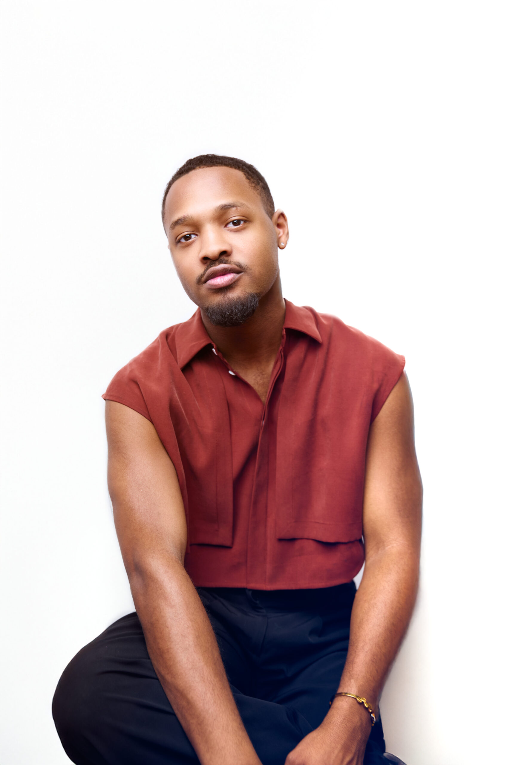 Headshot of Butler wearing a red top and navy pants, seated with one leg crossed and looking into the camera against a white background