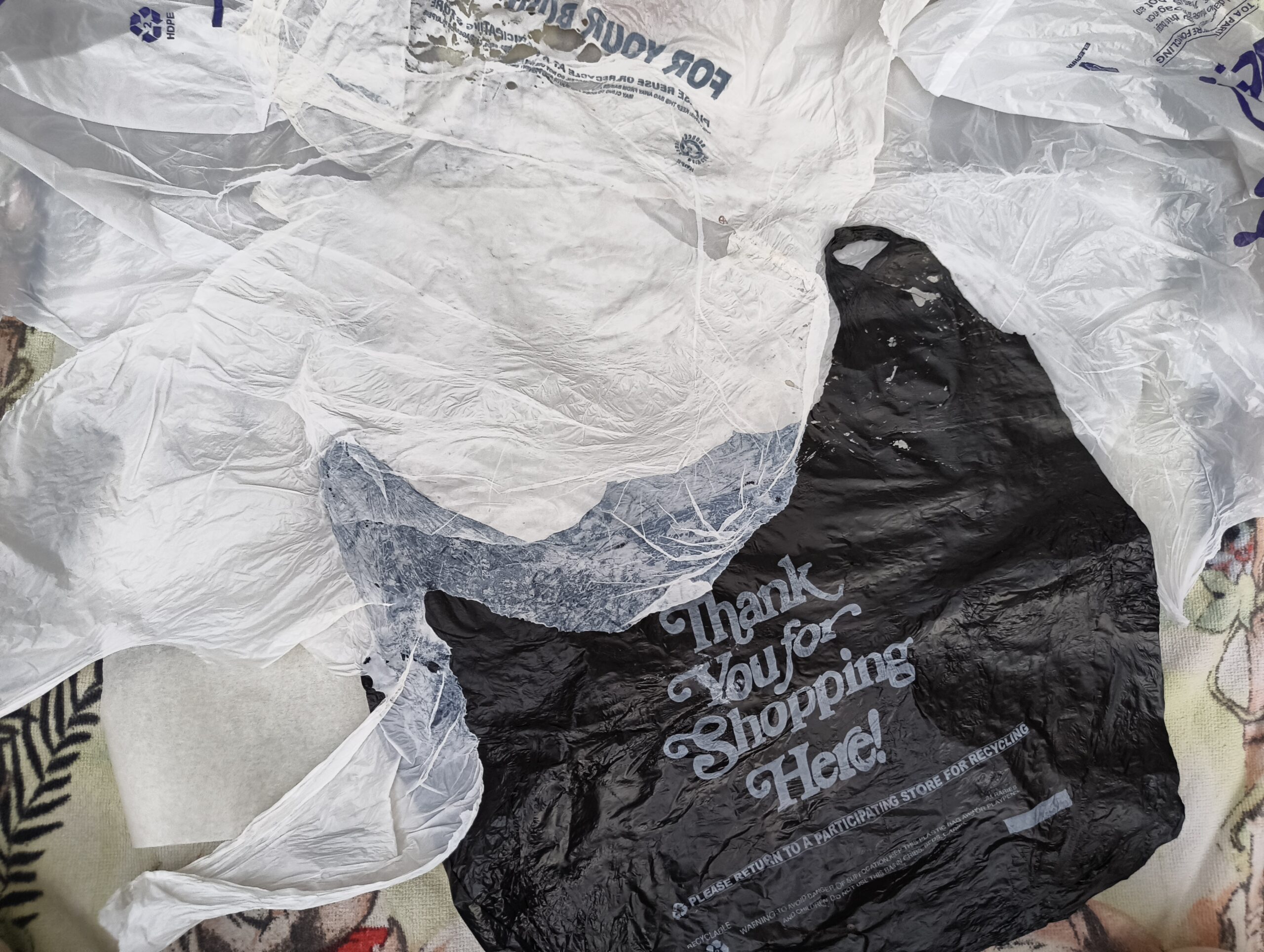 Several plastic shopping bags are scattered on a surface. The bags are mostly crumpled and include a white bag, a clear bag, and a black bag with the text 