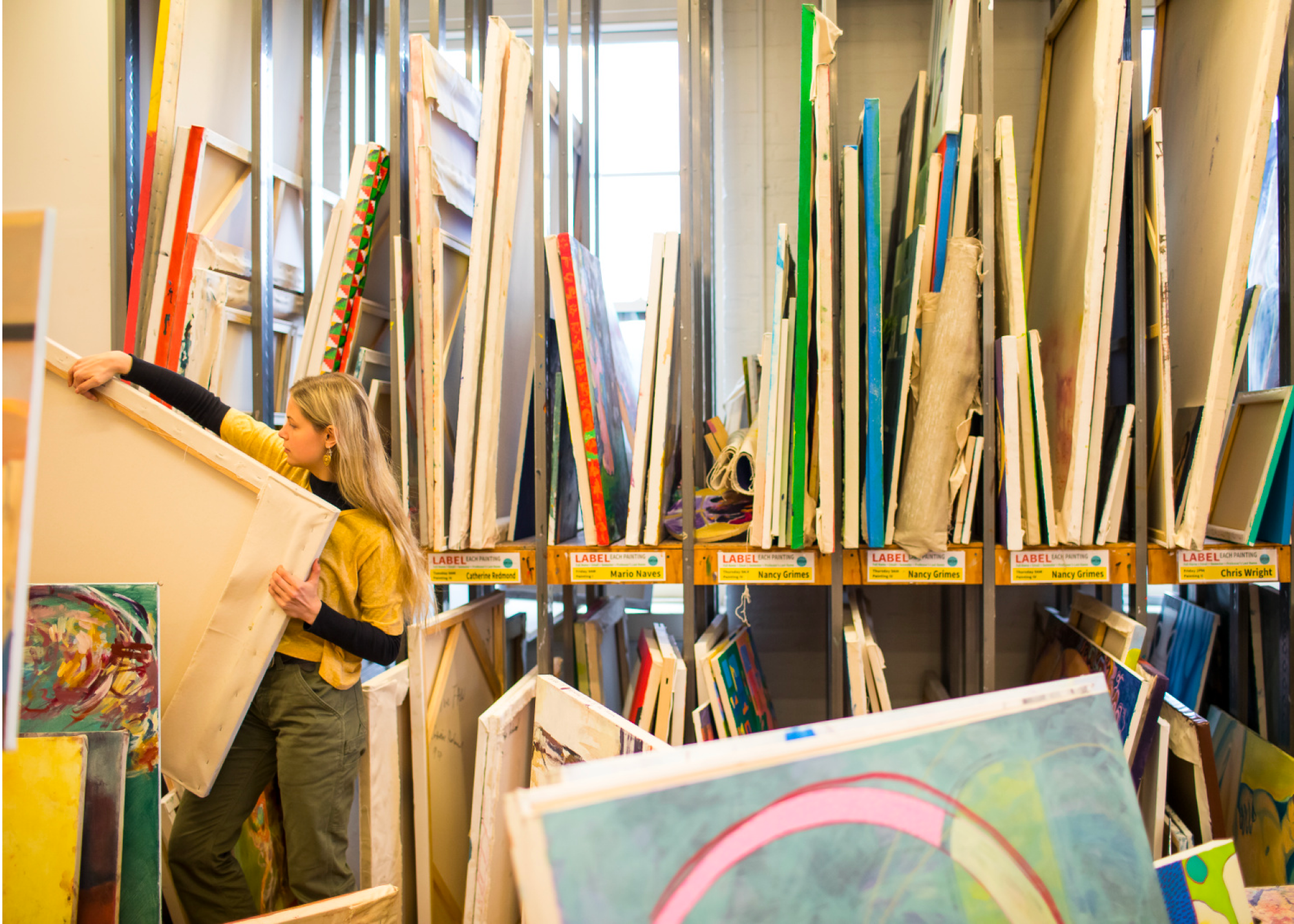 Shelves in a classroom holding different canvases and paintings.