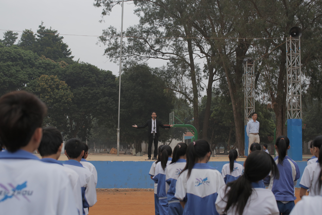 Person on a stage addressing students in unifrom.