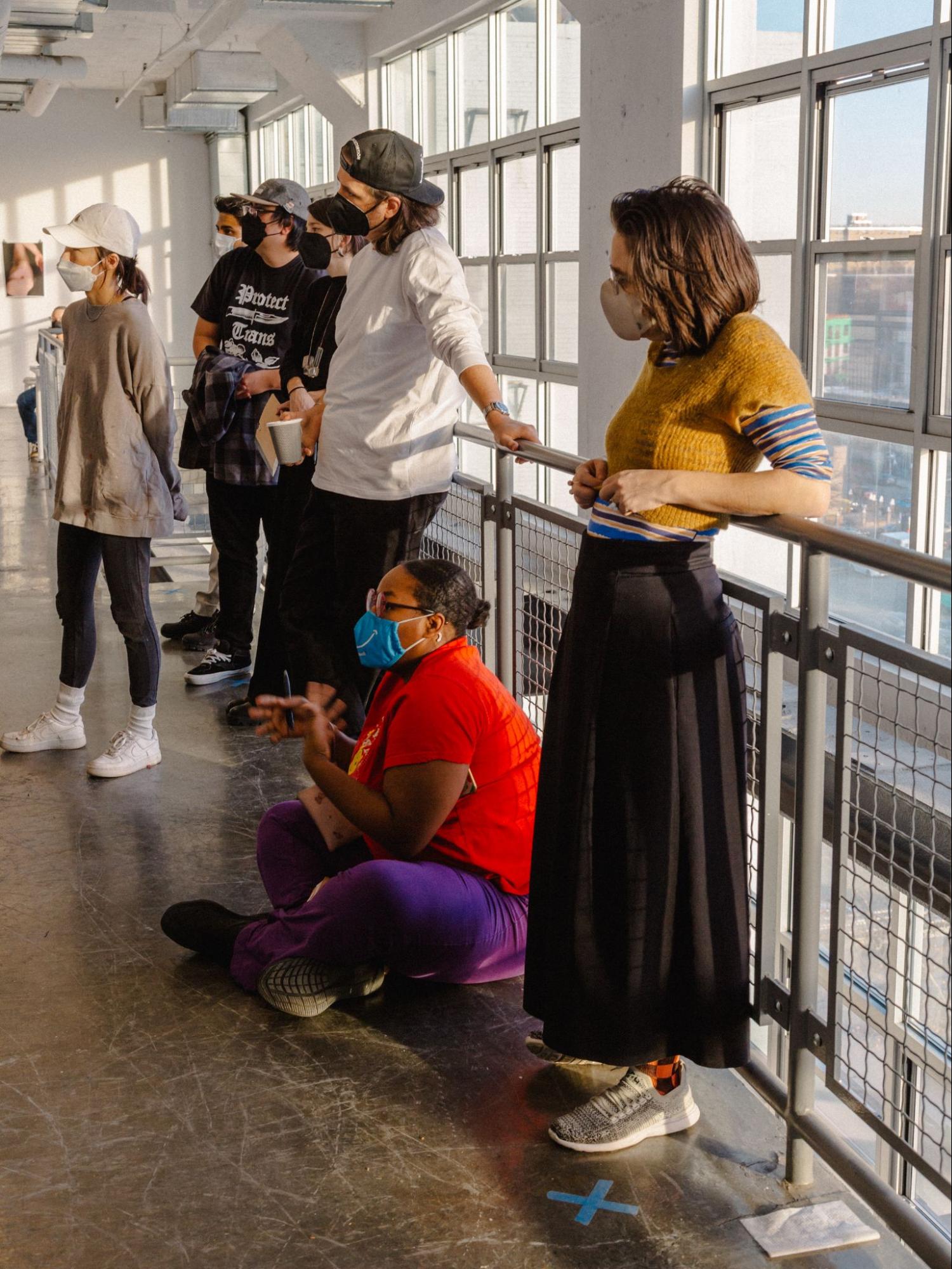 students standing on railing in hallway, masked, which appear to be listening to someone speak out of frame