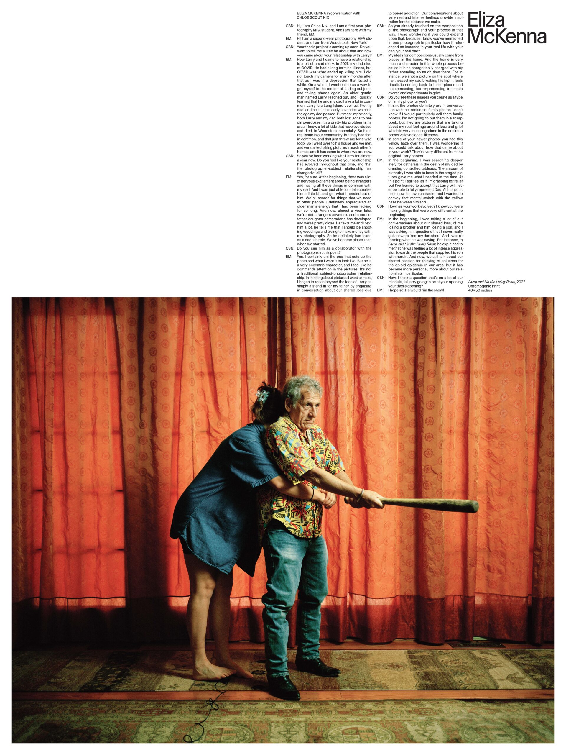 An older man holds a baseball bat straight out with both hands. He's wearing jeans and a brightly colored button-down short sleeve shirt. He's standing in a room in front of a large red curtain. A woman in a blue denim shirt is hugging him from behind. Her face is obscured.