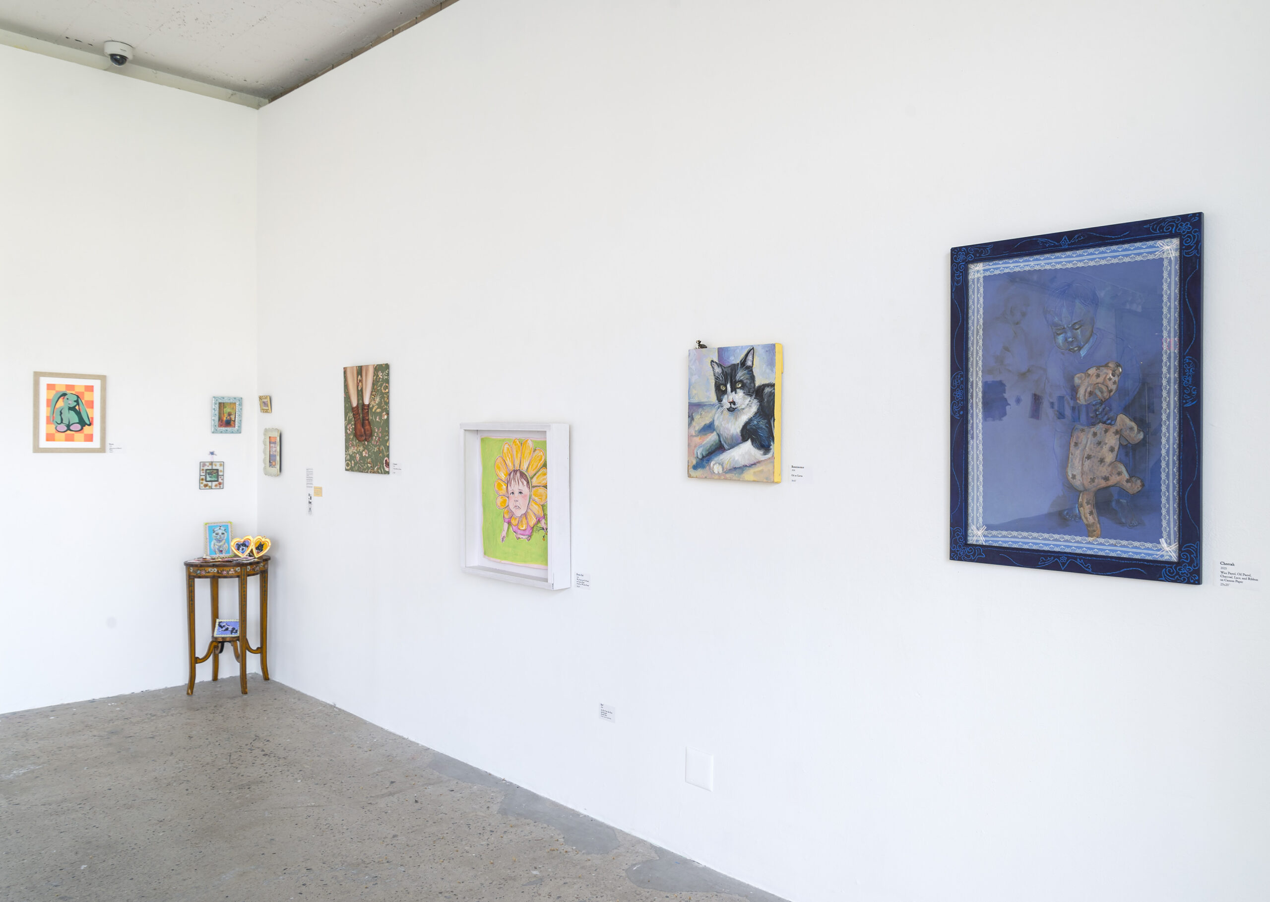 A gallery exhibition featuring a mix of surreal and urban-inspired paintings. On the left, a dramatic painting depicts a figure in a dark setting, while the right side showcases works exploring themes of city life, neon lights, and subway environments. The white walls and minimalist layout emphasize the vibrancy and detail of each piece.