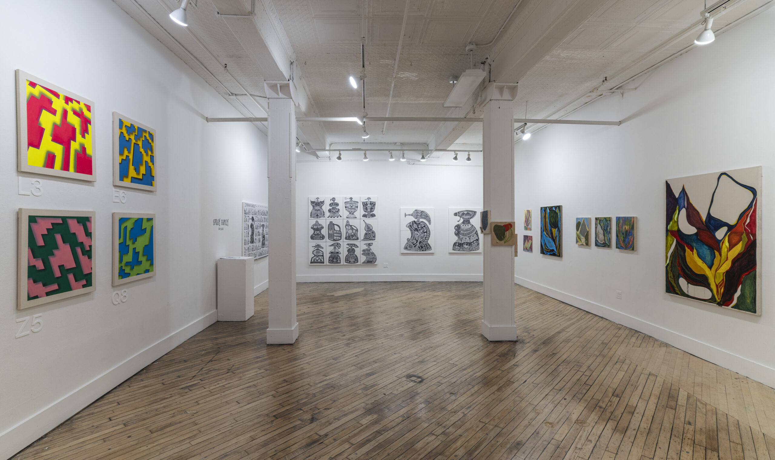 A modern art gallery with white walls and a polished wooden floor, displaying various abstract paintings. The artworks range from colorful, expressive brushstrokes to structured geometric designs. The gallery is well-lit, with spotlights accentuating each piece.