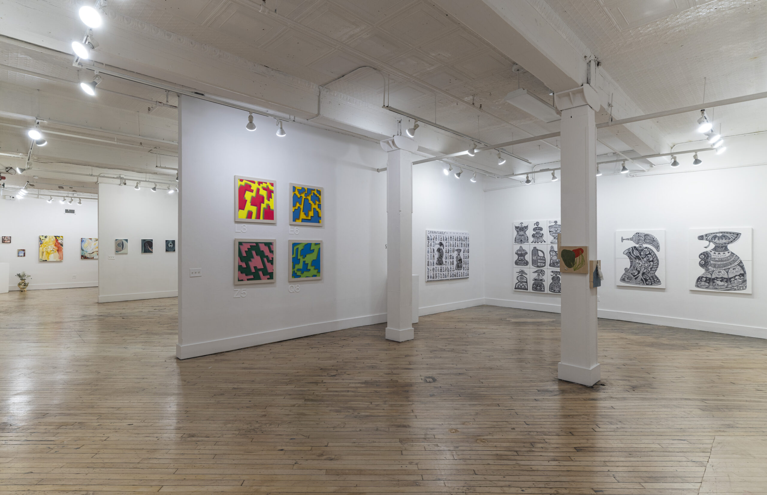 A minimalist art gallery room displaying a mix of small and medium-sized paintings. The pieces appear to be expressive, with some leaning toward abstract themes. The lighting setup consists of multiple spotlights, creating a focused ambiance for viewing the artwork.