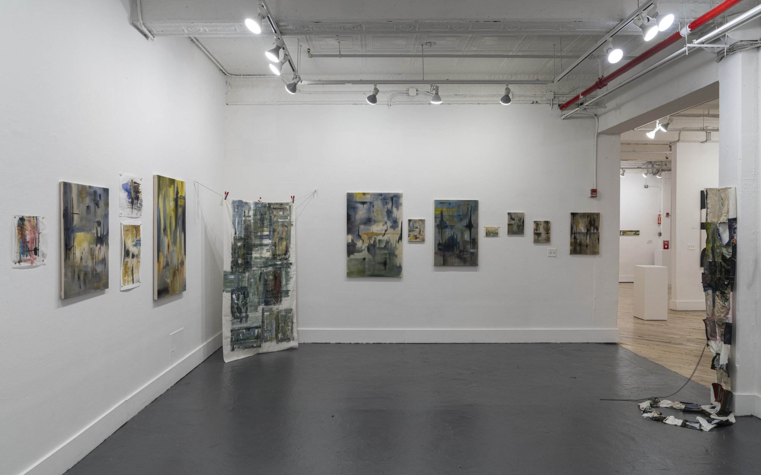 A well-lit art gallery featuring a mix of abstract paintings and surreal black-and-white illustrations. The polished wooden floor and high ceilings contribute to an open and spacious feel. The artwork is arranged in sections, allowing visitors to explore different artistic styles.