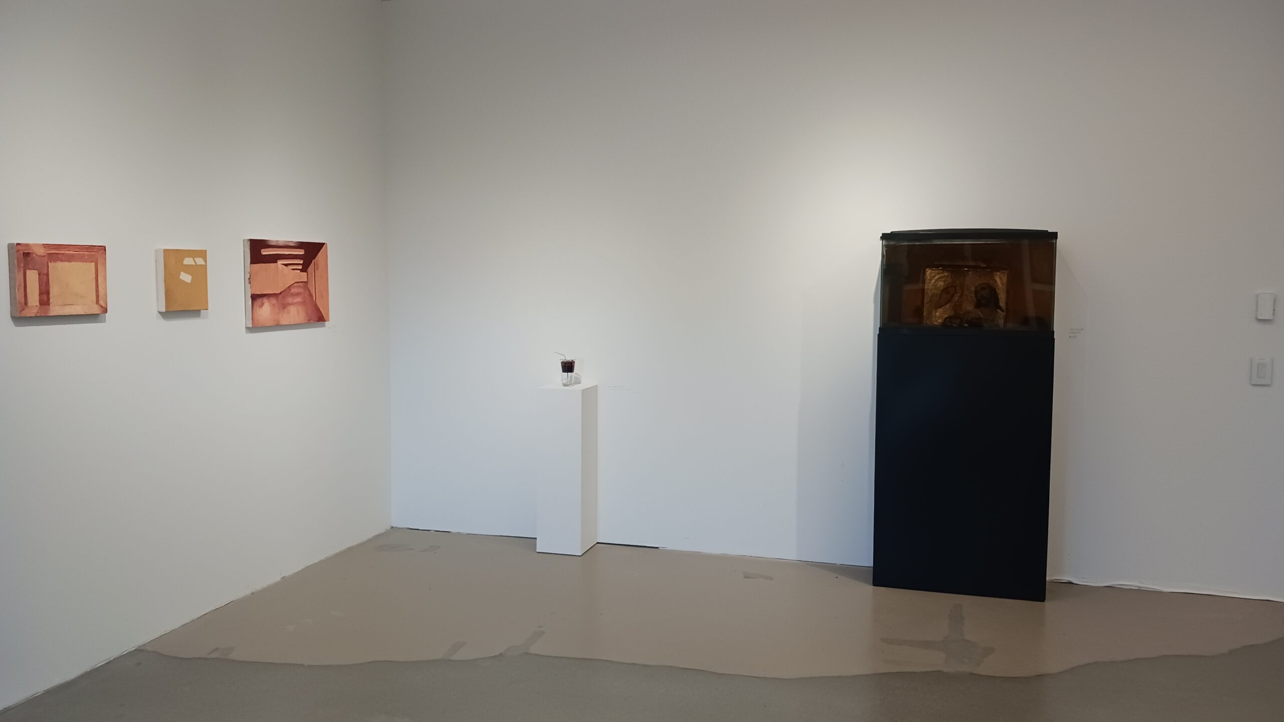 A contemporary art gallery featuring a mix of abstract and conceptual artworks. The foreground includes a large circular wooden shelving unit, a green and red children's bicycle, and a silver scooter lying on the floor. The walls display a variety of abstract geometric paintings, while a textured mixed-media canvas with sculptural elements hangs on the right. The space has an industrial ceiling with exposed beams and a polished concrete floor.